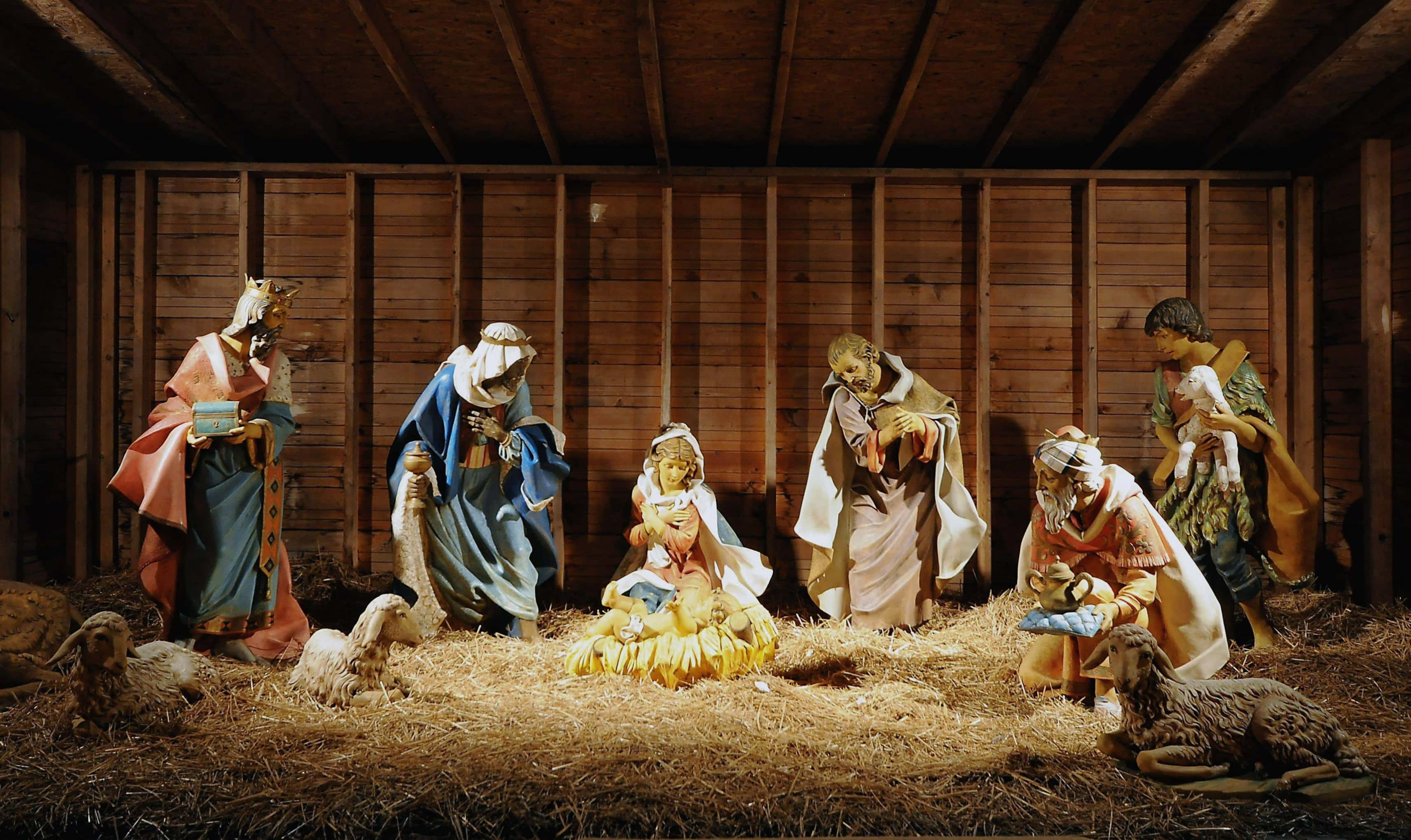 Nativity 桌布 壁紙 — 一個溫暖照亮的耶穌誕生場景，有瑪利亞、約瑟、嬰兒耶穌、牧羊人和動物的小雕像，位於質樸的木製馬廄中。