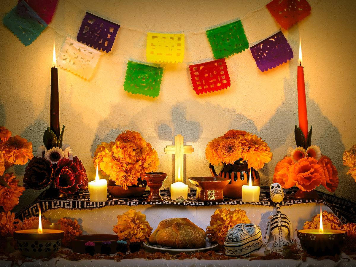 Dia De Los Muertos 桌布 壁紙 — 一個溫暖照明的亡靈節祭壇，裝飾著萬壽菊、蠟燭、糖骷髏和色彩繽紛的 papel picado 橫幅。