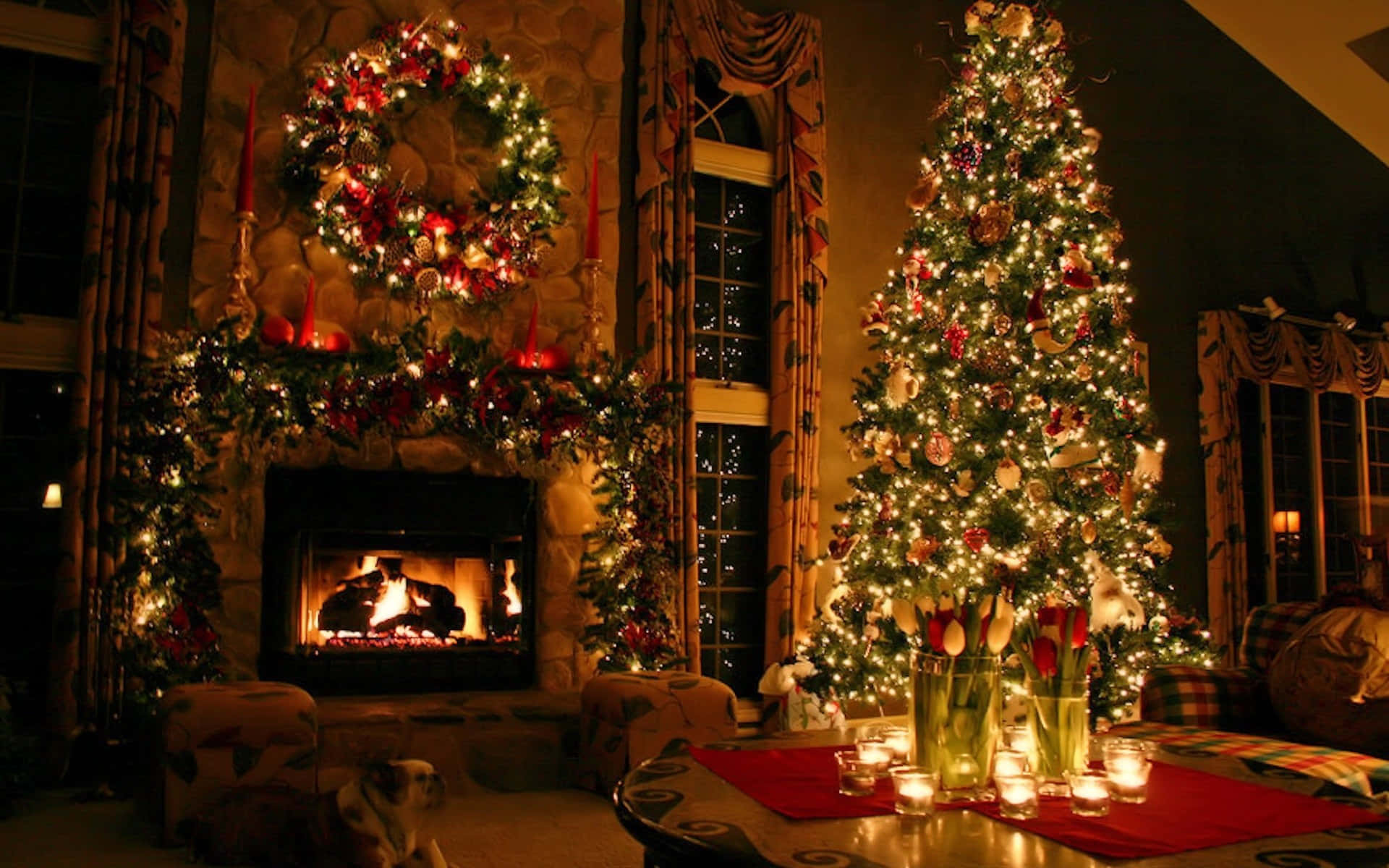 Christmas At Hogwarts 桌布 壁紙 — 一個溫暖照明的客廳，設有一個閃爍的壁爐，裝飾著節日花環，還有一棵高大的裝飾聖誕樹，掛滿閃爍的燈光和裝飾品。