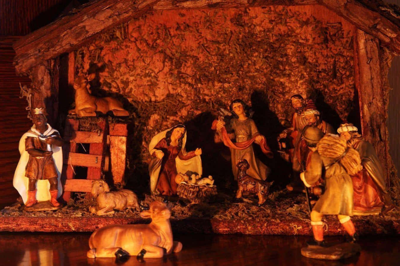 Nativity 桌布 壁紙 — 一個溫暖照明的耶穌誕生場景，有瑪利亞、約瑟、嬰兒耶穌、牧羊人和動物的雕像，在質樸的木屋頂下。