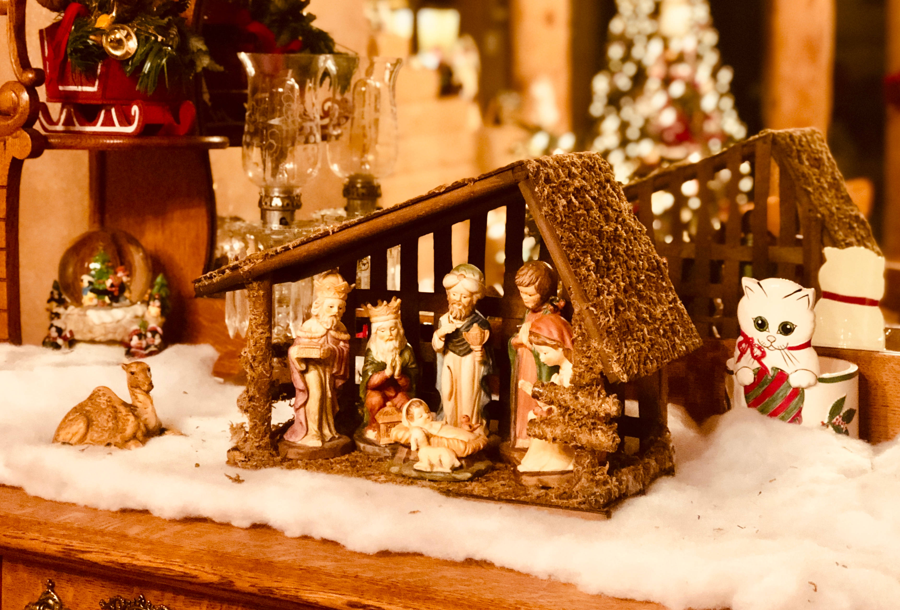 Nativity 桌布 壁紙 — 一個溫暖照明的聖誕馬槽場景，木架上擺放著人偶和假雪，周圍環繞著節日裝飾。