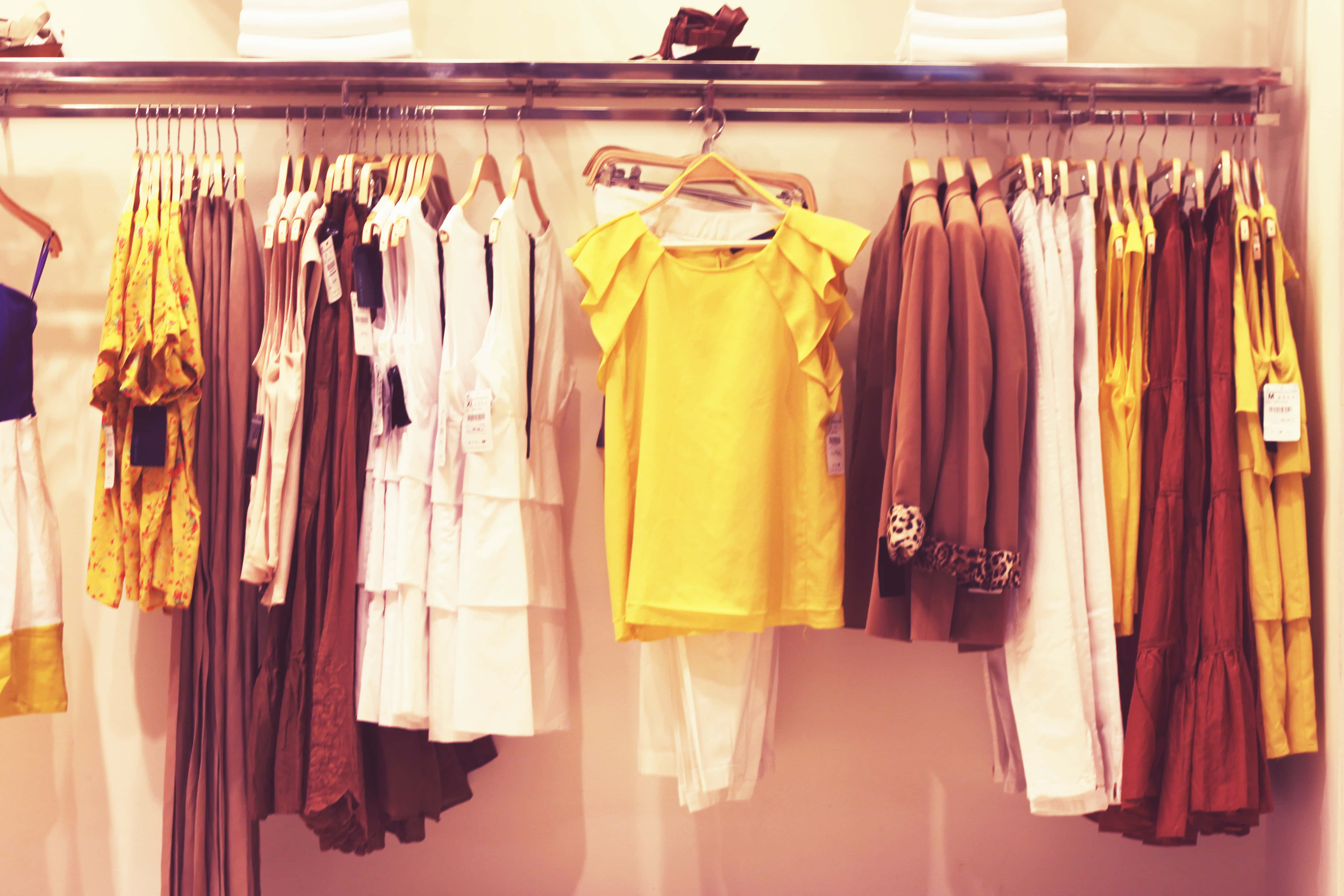 Clothes 桌布 壁紙 — 一個溫暖照明的衣架上展示著色彩繽紛的衣物，包括一件亮黃色上衣和大地色調的連衣裙。