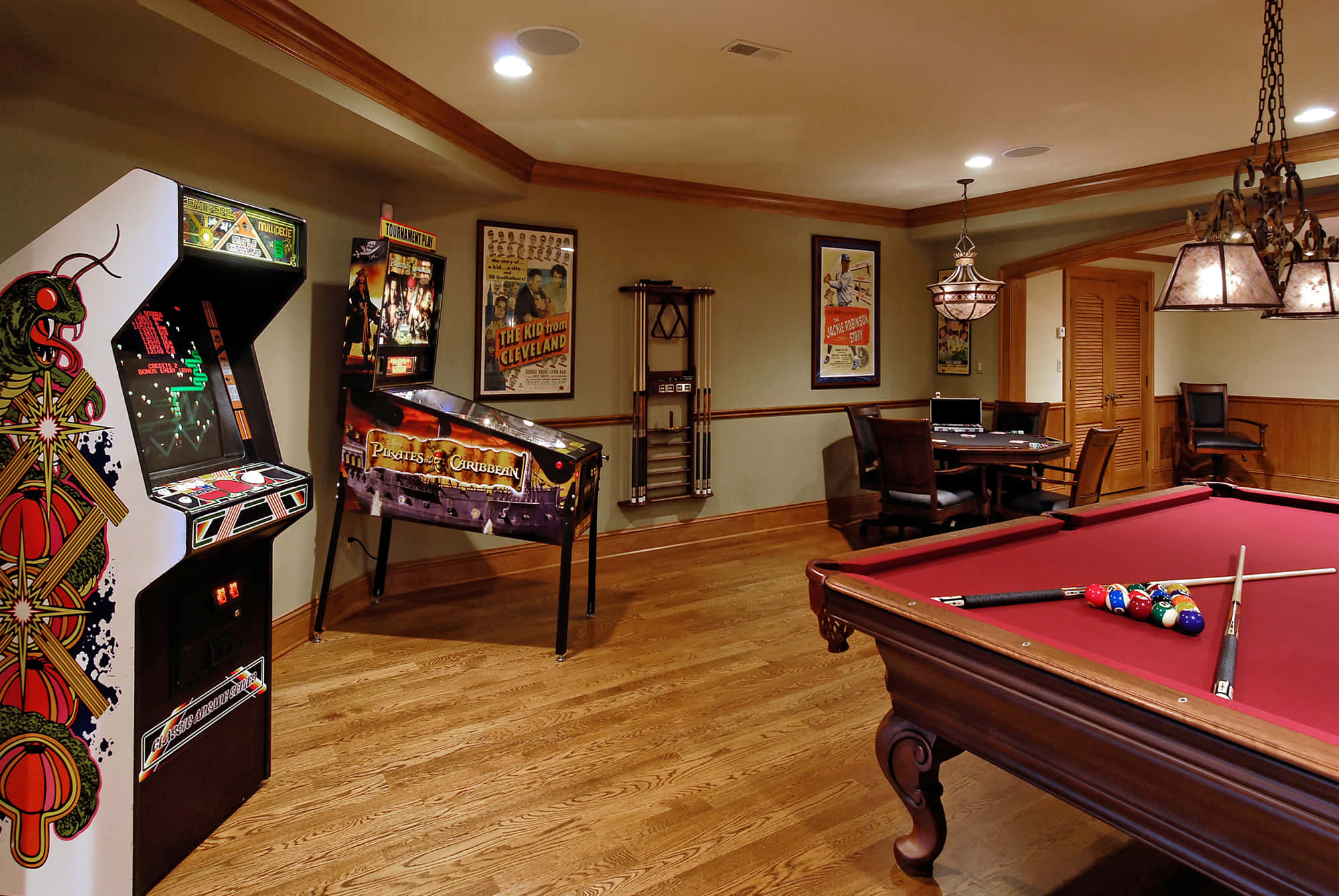 Game Room 桌布 壁紙 — 一個溫暖照明的遊戲室，裝飾華麗的吊燈下有一張紅色撞球桌、復古街機和彈珠機。