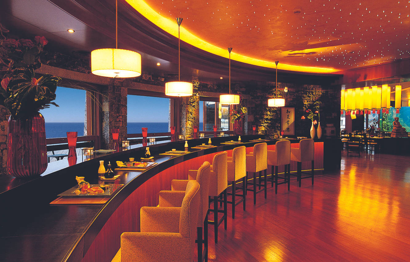 Hotel 桌布 壁紙 — 一個溫暖燈光的弧形酒吧，配有琥珀色燈光和黃昏時分的海景。