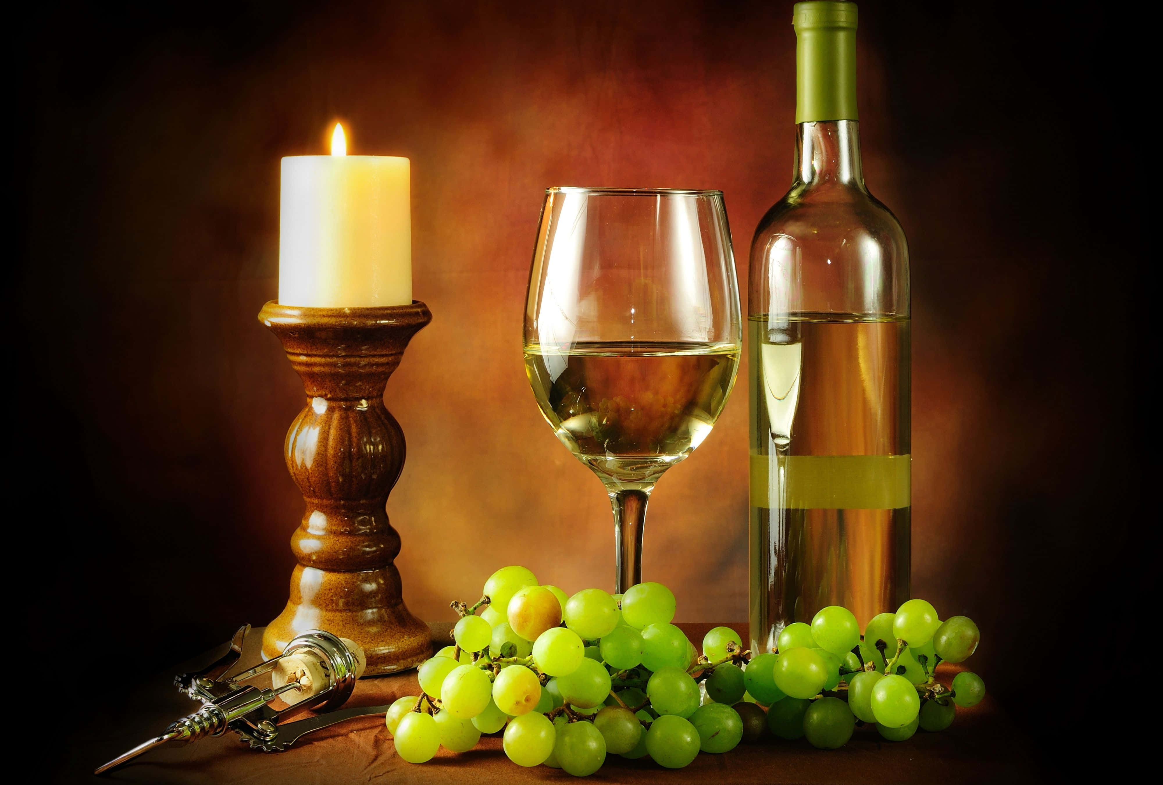 White Wine 桌布 壁紙 — 一個溫暖燈光的靜物擺設，包含蠟燭、酒瓶、玻璃杯和新鮮青葡萄，置於木質表面上。