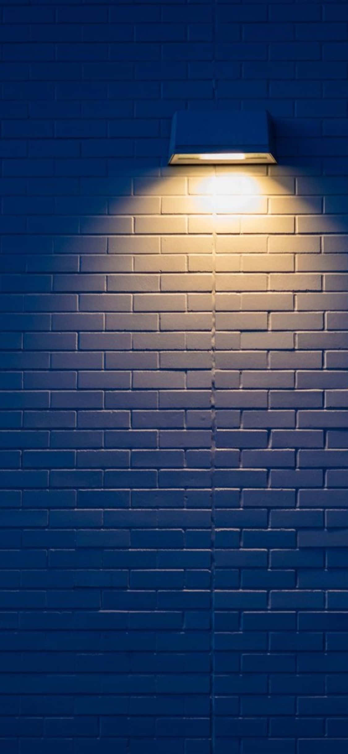 Brick Wall 桌布 壁紙 — 一個溫暖發光的戶外燈具在夜間將柔和的光圈投射在深藍色磚牆上。