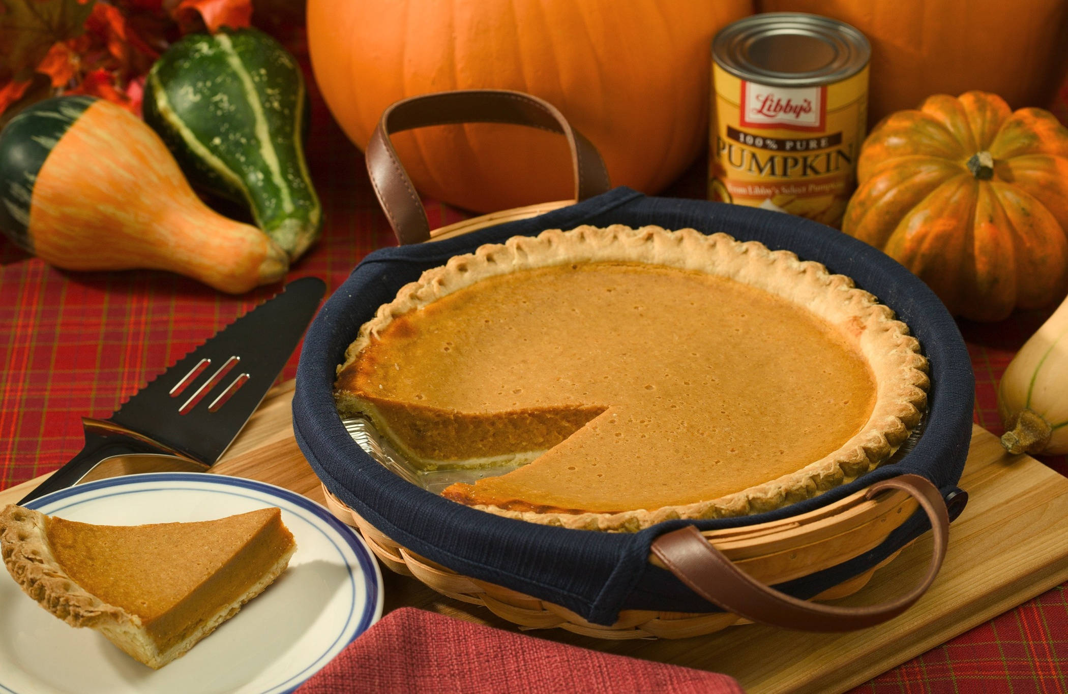 Pie 桌布 壁紙 — 一個溫暖的南瓜派，附有一片放在盤子上，周圍有南瓜、葫蘆和 Libby's 南瓜罐頭，放在格子桌布上。