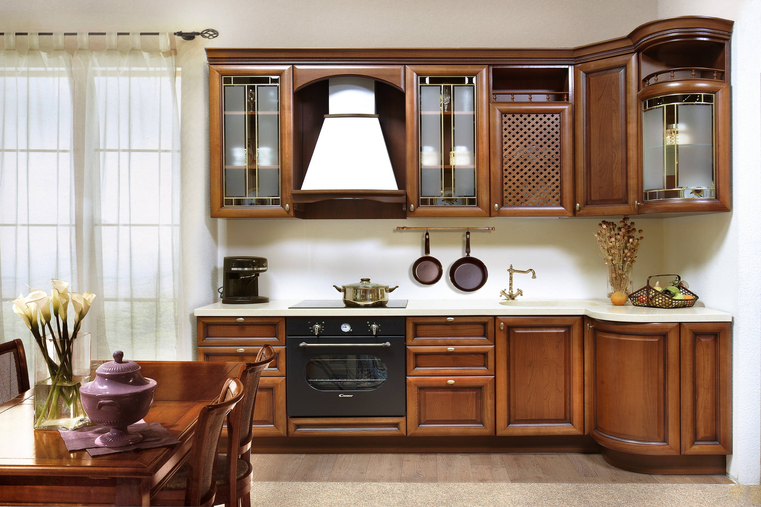 Kitchen Design 桌布 壁紙 — 一個溫暖的木質廚房，配有豐富的棕色櫥櫃、玻璃門上層櫃，以及靠近帶有薄紗窗簾的窗戶的餐桌。