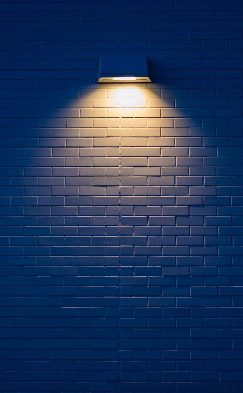images 桌布 壁紙 — 一個溫暖的燈具在夜晚將發光的圓圈投射在深藍色的磚牆上。