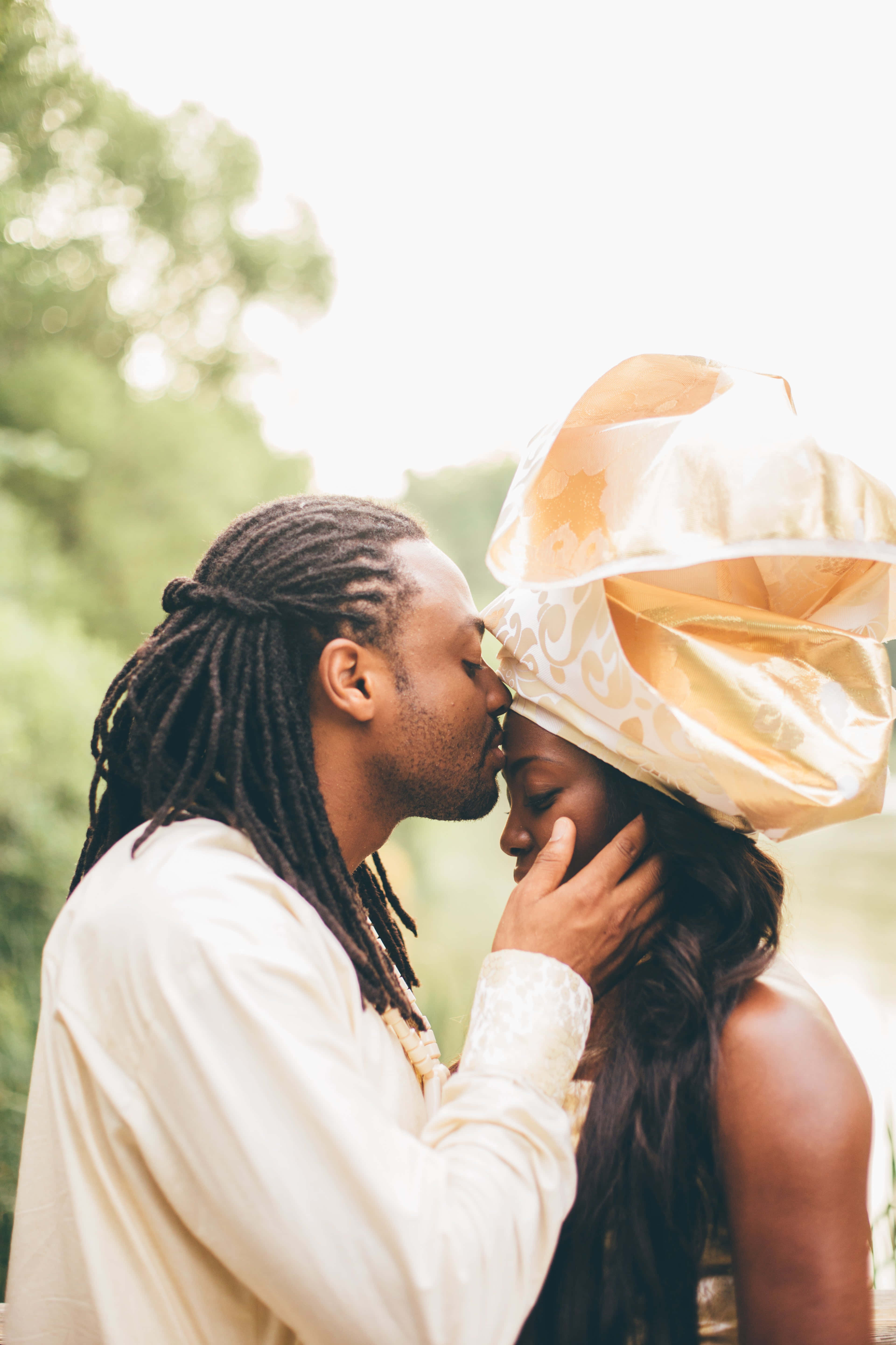 Forehead Kiss 桌布 壁紙 — 一個溫柔的時刻，一個男人親吻一個女人的額頭，而她戴著金色圖案的頭巾在戶外。