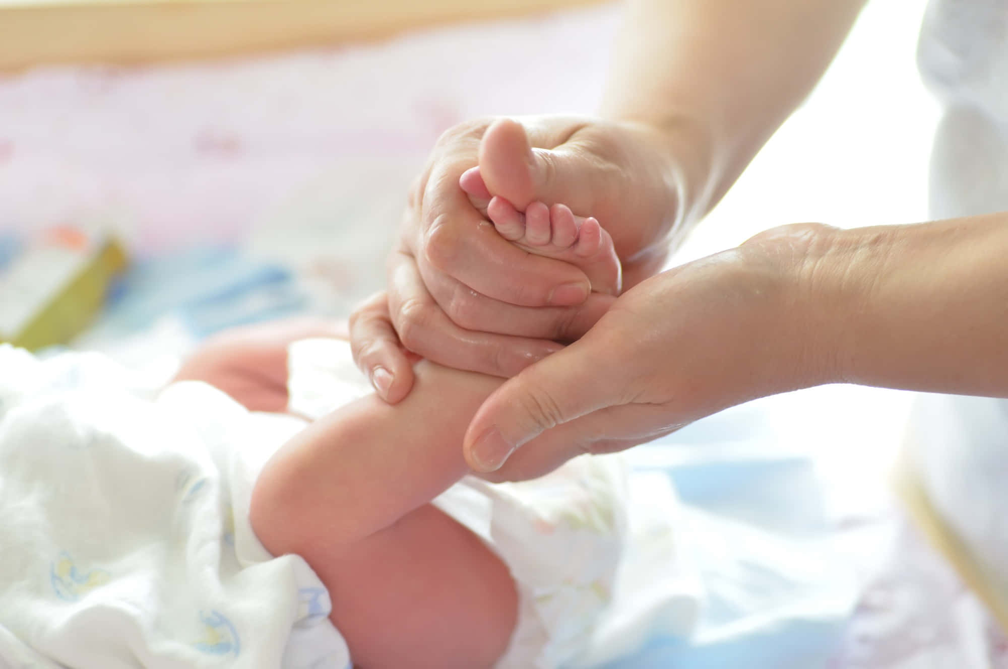 Massage 桌布 壁紙 — 一個溫柔的時刻，成年人的手輕輕地捧著新生嬰兒的小腳，包裹在柔軟的白色毯子裡。