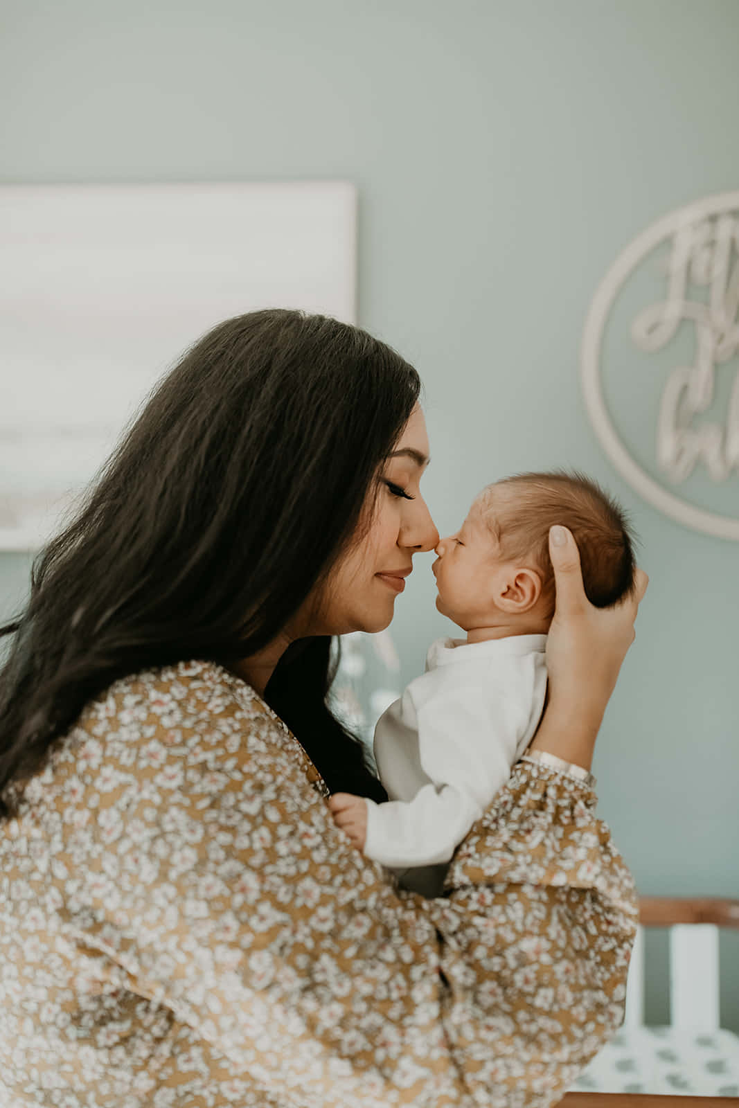 Newborn Baby 桌布 壁紙 — 一個溫柔的時刻，母親在柔和光線的嬰兒房裡輕輕親吻她初生嬰兒的額頭。