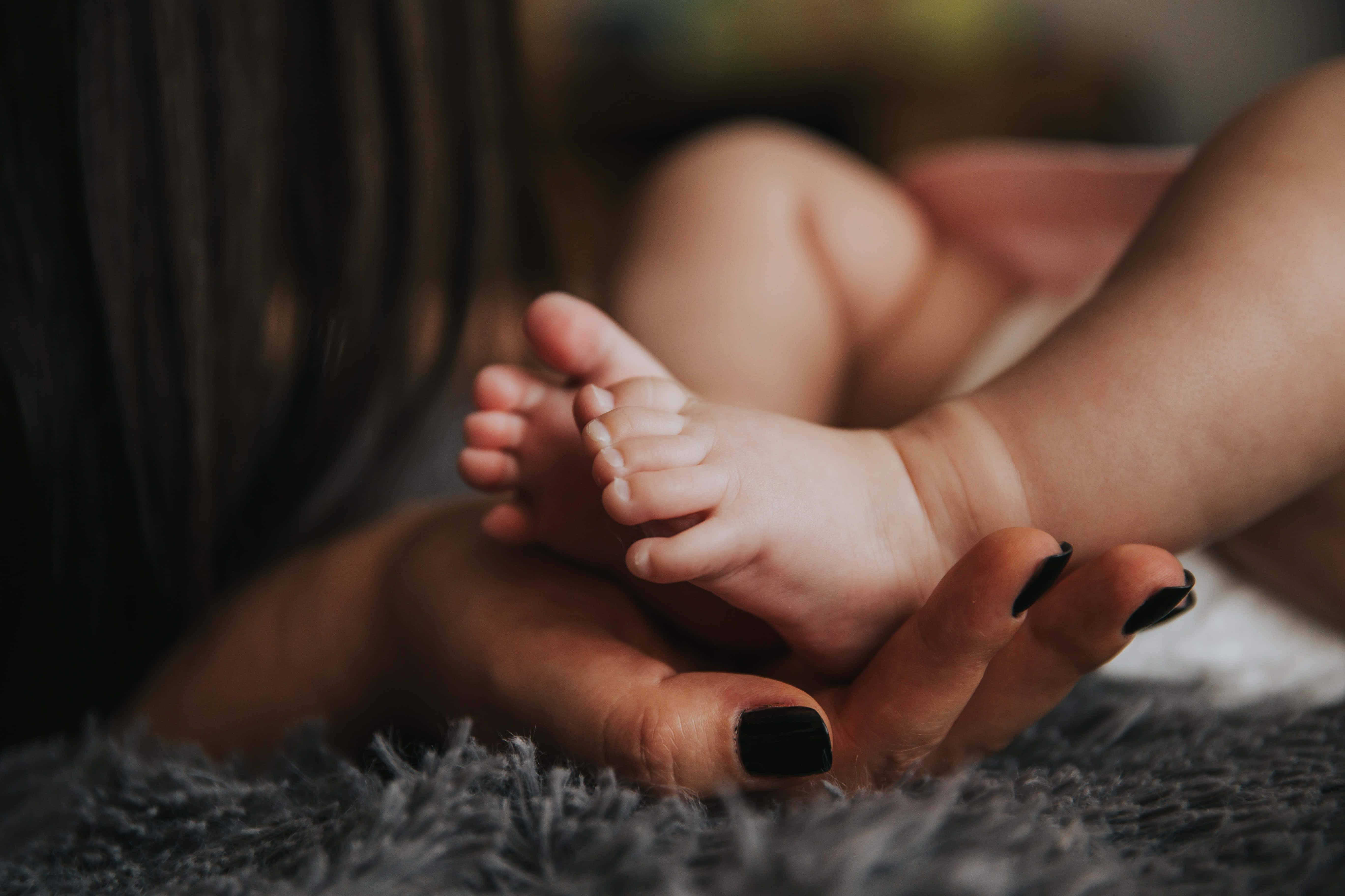 Mom 桌布 壁紙 — 一個溫柔的特寫，成年人的雙手在柔軟的灰色地毯上輕托著嬰兒的小腳。