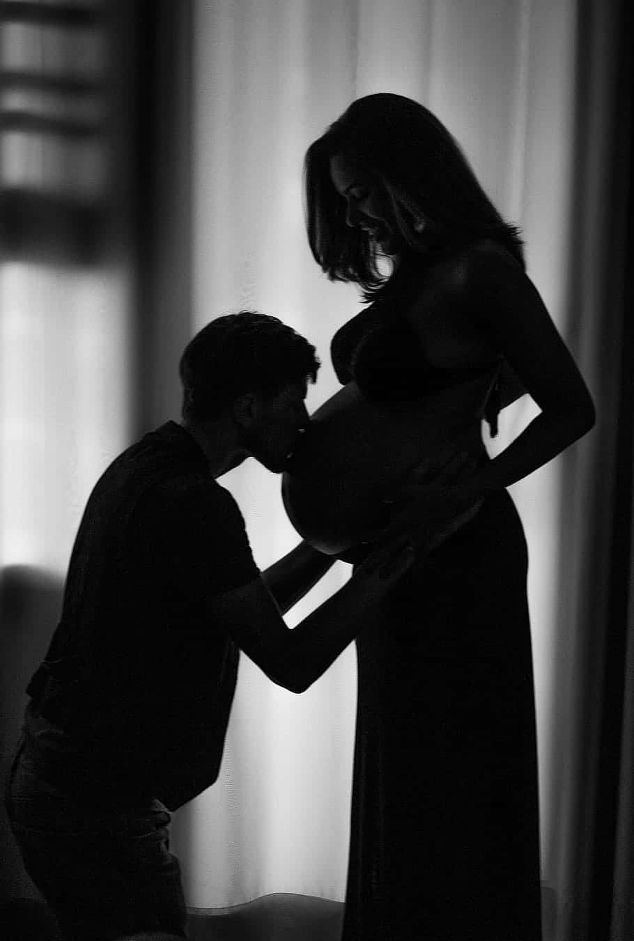 Silhouette 桌布 壁紙 — 一個溫柔的黑白剪影，描繪一名男子親吻一位站在窗邊的孕婦的肚子。