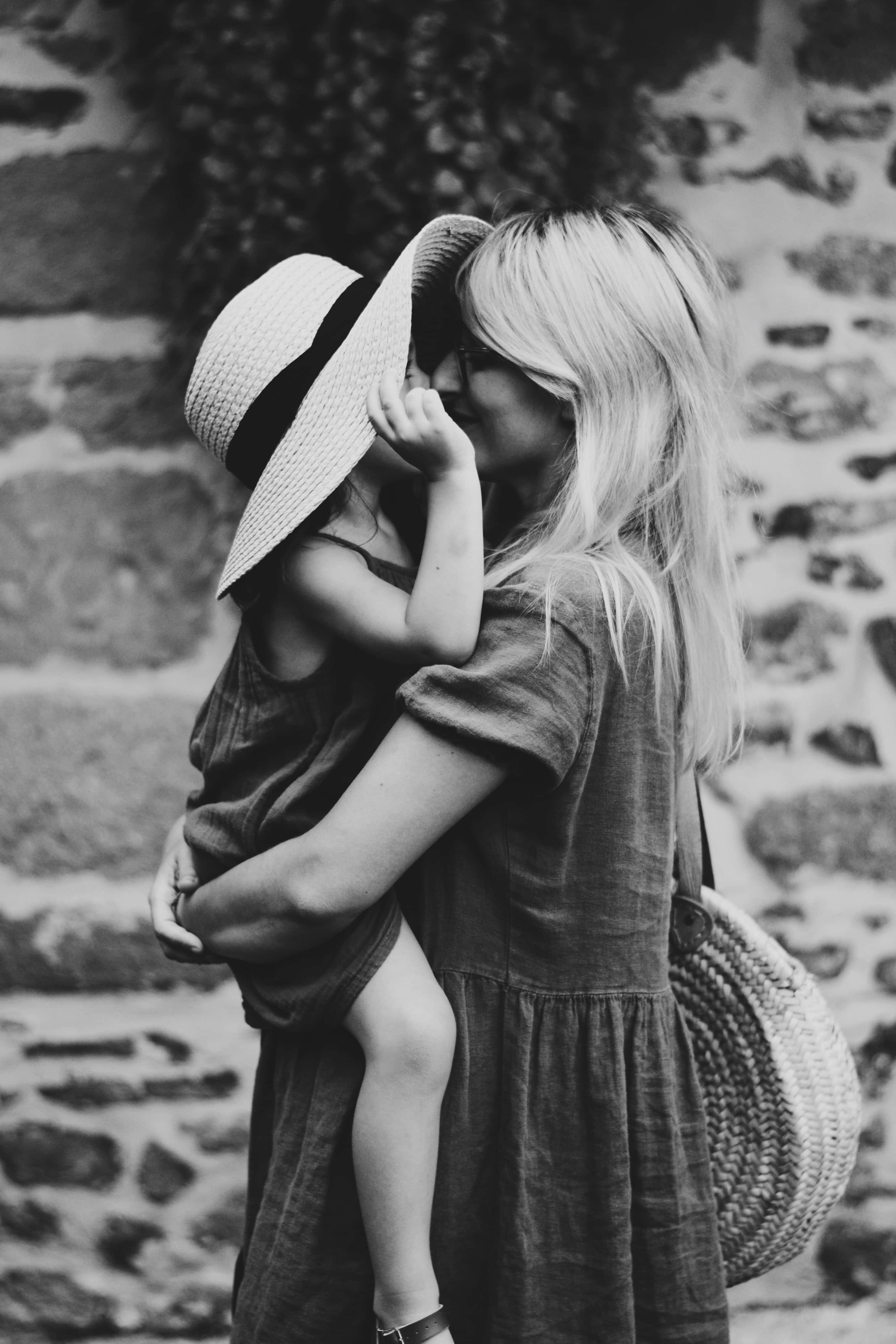 mother 桌布 壁紙 — 一個溫柔的黑白瞬間，一位女士在石牆前擁抱一個戴著寬邊帽的孩子。