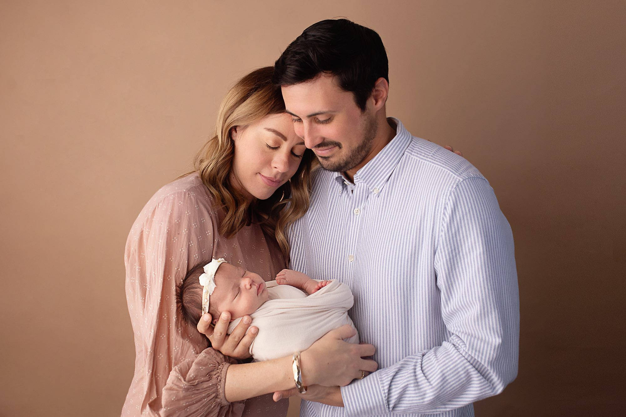 Mom 桌布 壁紙 — 一個溫馨的時刻，一個新的三口之家在柔和的攝影棚燈光下，在溫暖的棕色背景前擁抱。