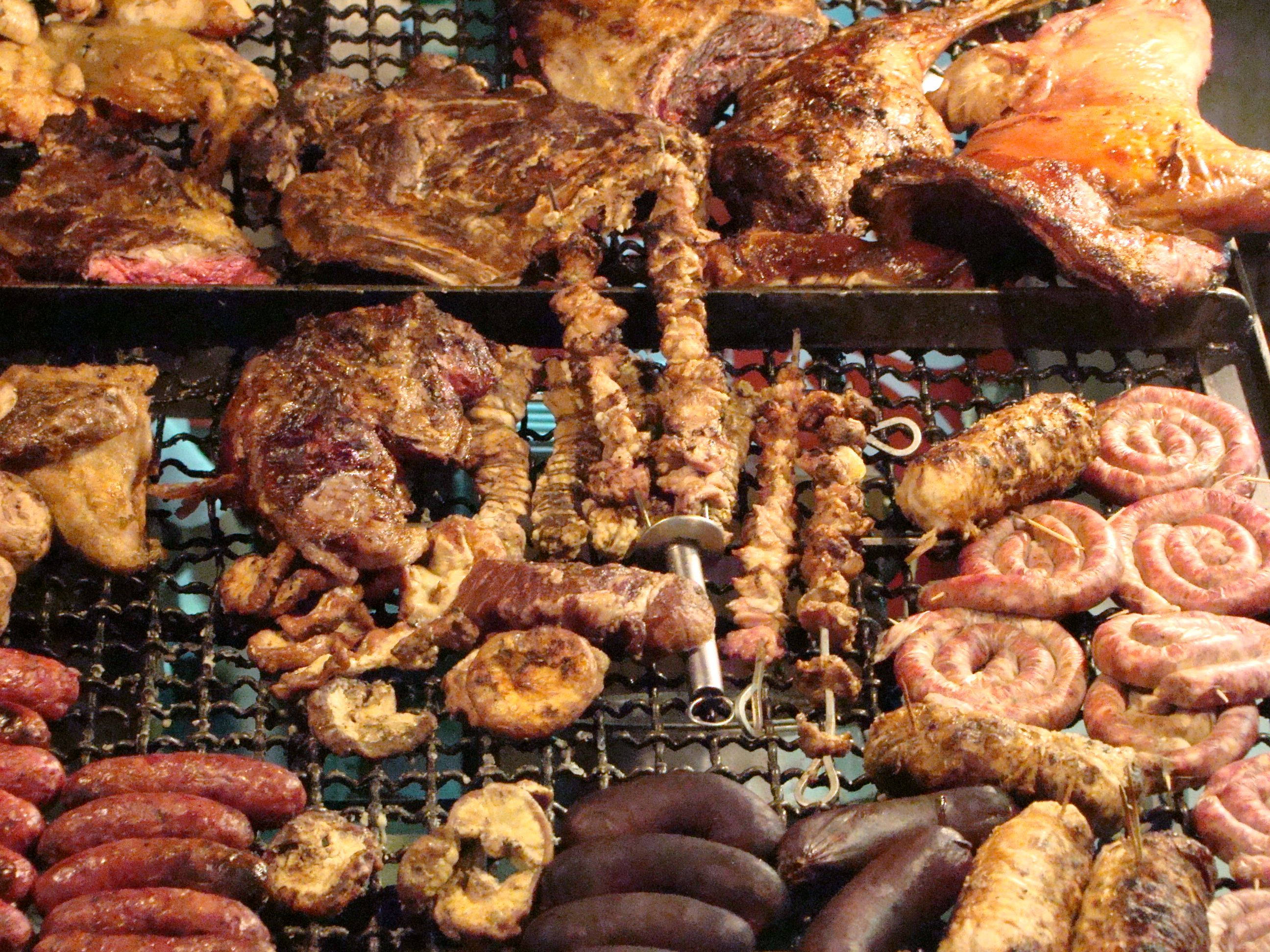 meat 桌布 壁紙 — 一個滋滋作響的烤架，上面放滿了各種肉類，包括肋骨、串燒、香腸和雞塊，在熾熱的炭火上烹煮。
