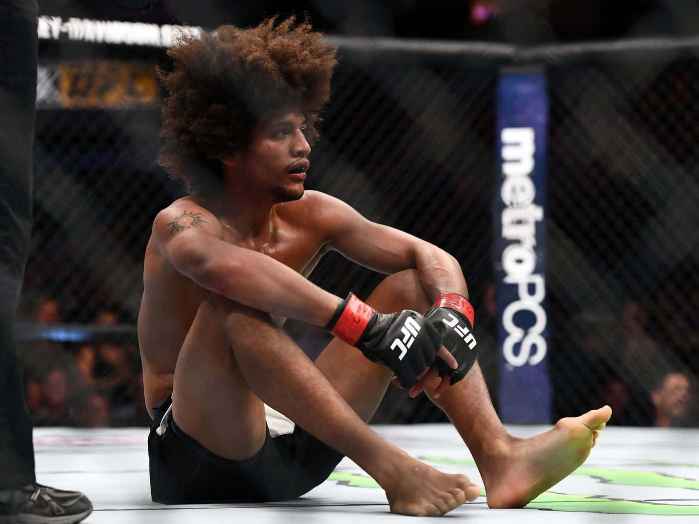 MMA 桌布 壁紙 — 一個滿身大汗、留著非洲式髮型的拳手坐在八角籠地上，在殘酷的MMA比賽後顯得筋疲力盡。