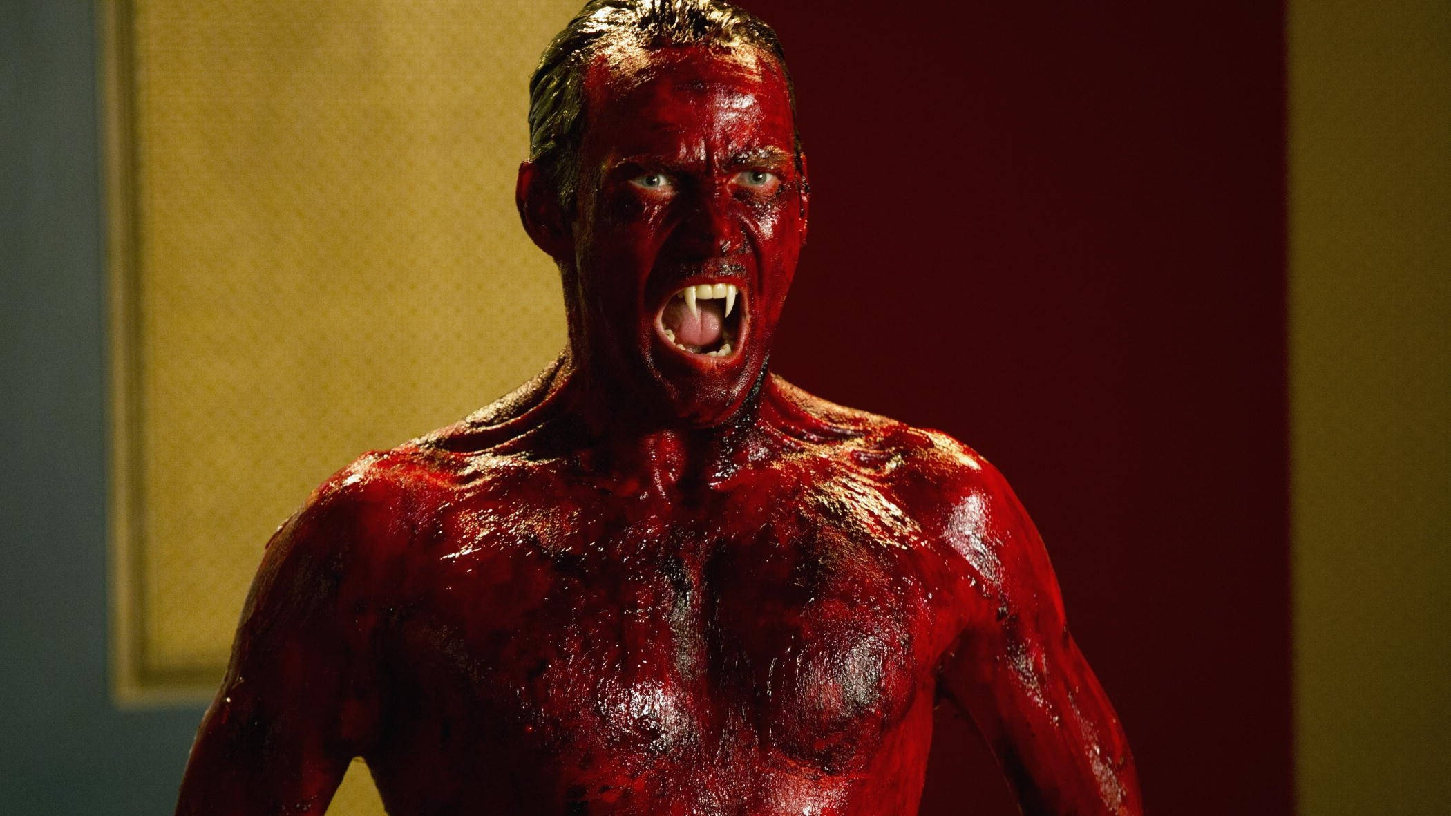 True Blood 桌布 壁紙 — 一個滿身鮮血、長有獠牙的男人在一個光線昏暗、牆壁黃紅相間的房間裡咆哮。