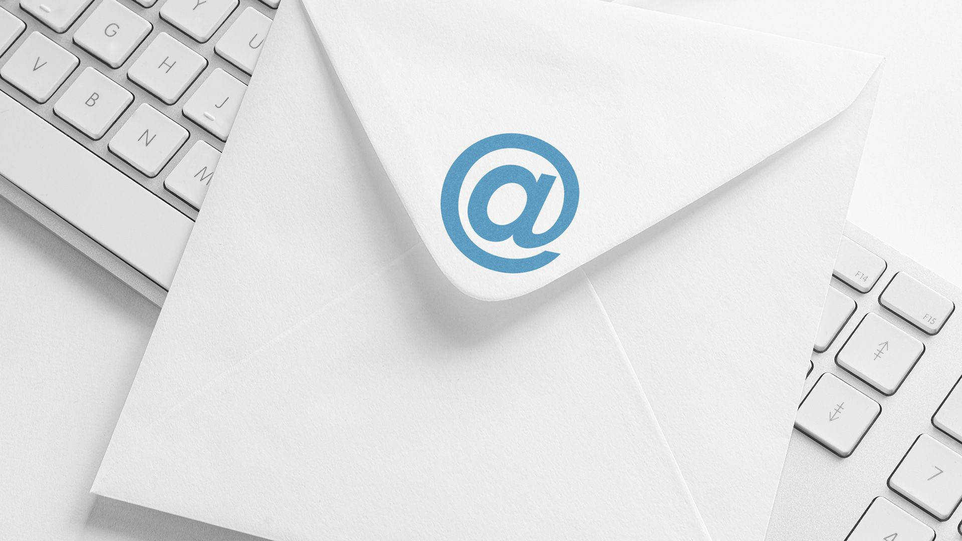 Email 桌布 壁紙 — 一個潔白的信封，上面有一個藍色的 @ 標誌，放在一個簡約工作空間的時尚白色鍵盤上。