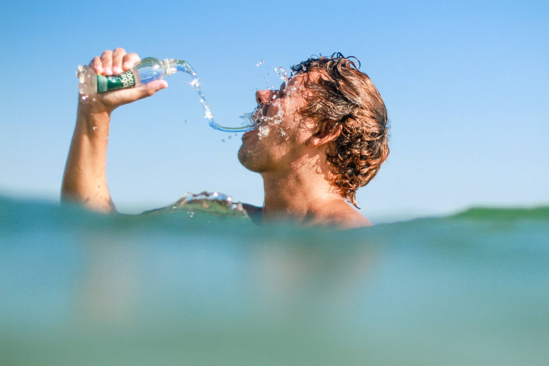 Drinking 桌布 壁紙 — 一個濕漉漉的捲髮男子半身浸在碧藍的海洋中，在清澈的藍天下從水瓶中喝水。