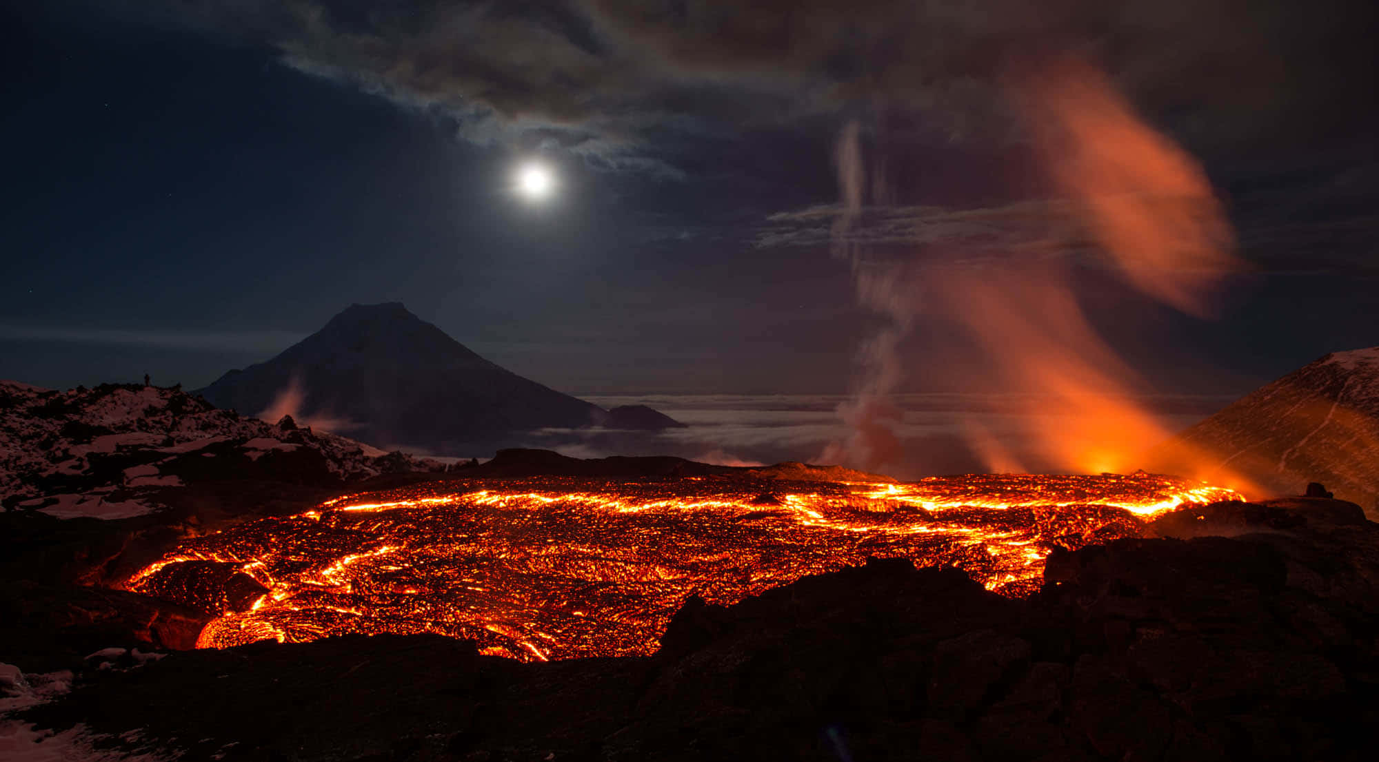 Volcano 桌布 壁紙 — 一個火山口在明亮的月光天空下，熔岩發光，山峰上覆蓋著雪。