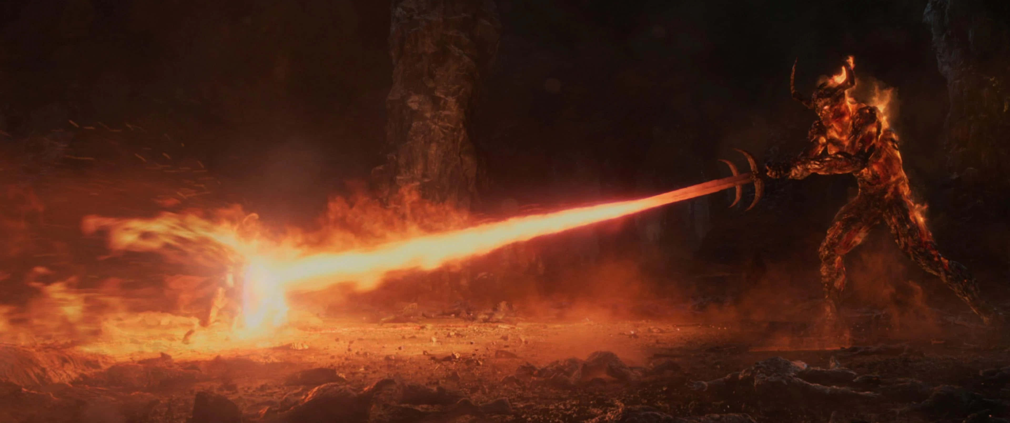 Surtur 桌布 壁紙 — 一個火焰惡魔在火山洞穴中揮舞著燃燒的劍，在岩石地形上投射出強烈的橙色光芒。