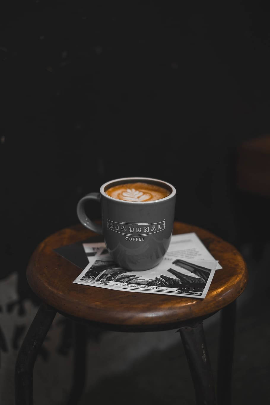 Coffee Shop 桌布 壁紙 — 一個灰色咖啡杯帶有拿鐵藝術，放在木凳上，凳下是一張黑白照片。