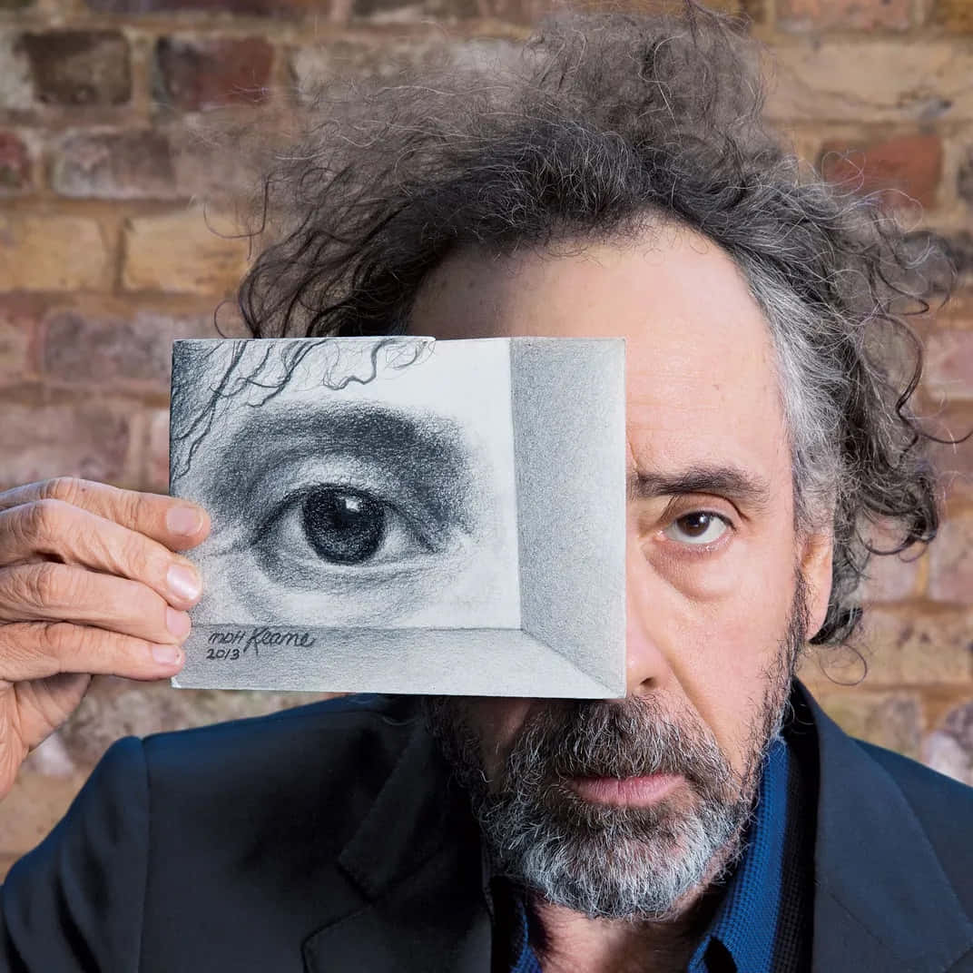 tim burton 桌布 壁紙 — 一個灰色捲髮的男人，在磚牆背景下，將一幅詳細的眼睛鉛筆畫舉在臉前。