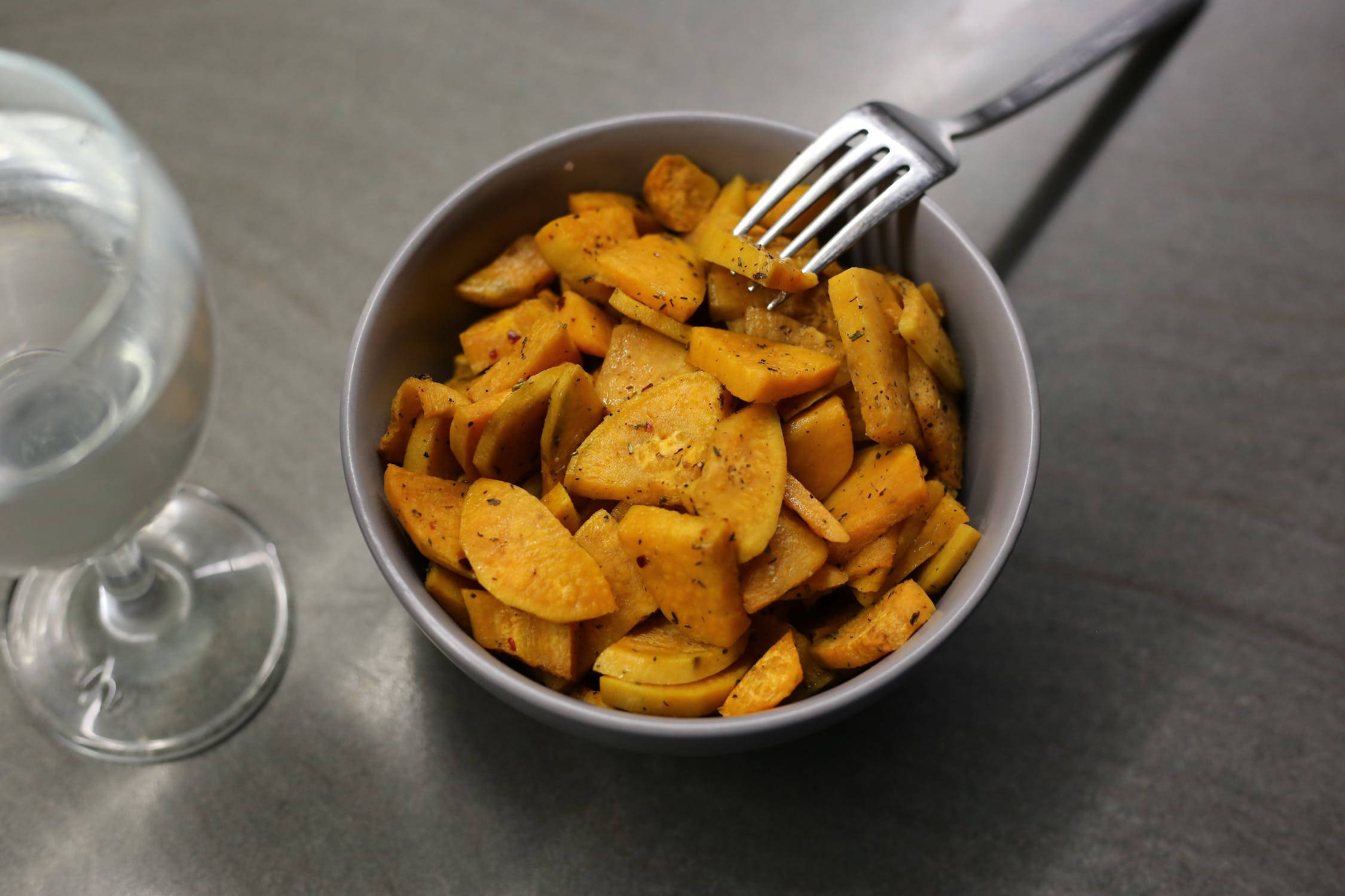 Healthy Food 桌布 壁紙 — 一個灰色桌面上，有一碗烤地瓜片，旁邊有叉子和一杯水。