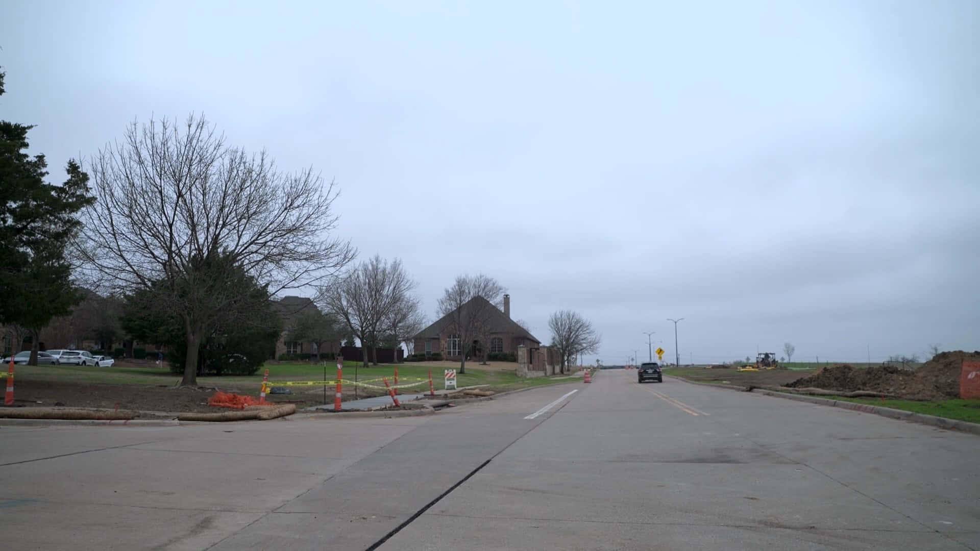 Neighborhood 桌布 壁紙 — 一個灰色的陰天顯示一條正在施工的道路，有橙色錐體和一座被光禿樹木包圍的遠處房屋。