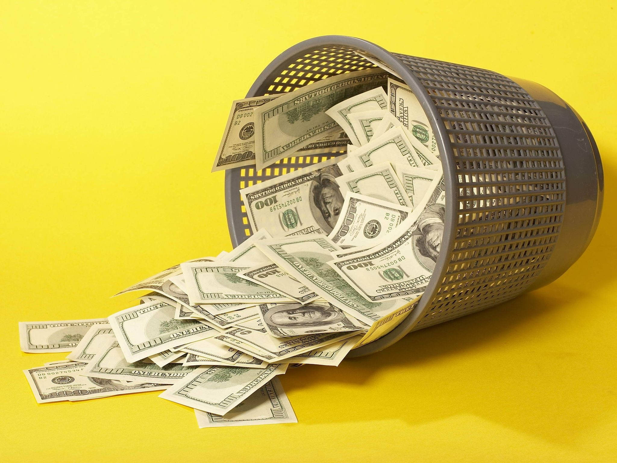 No Money 桌布 壁紙 — 一個灰色穿孔垃圾桶倒在明亮的黃色背景上，灑出皺巴巴的百元美鈔。