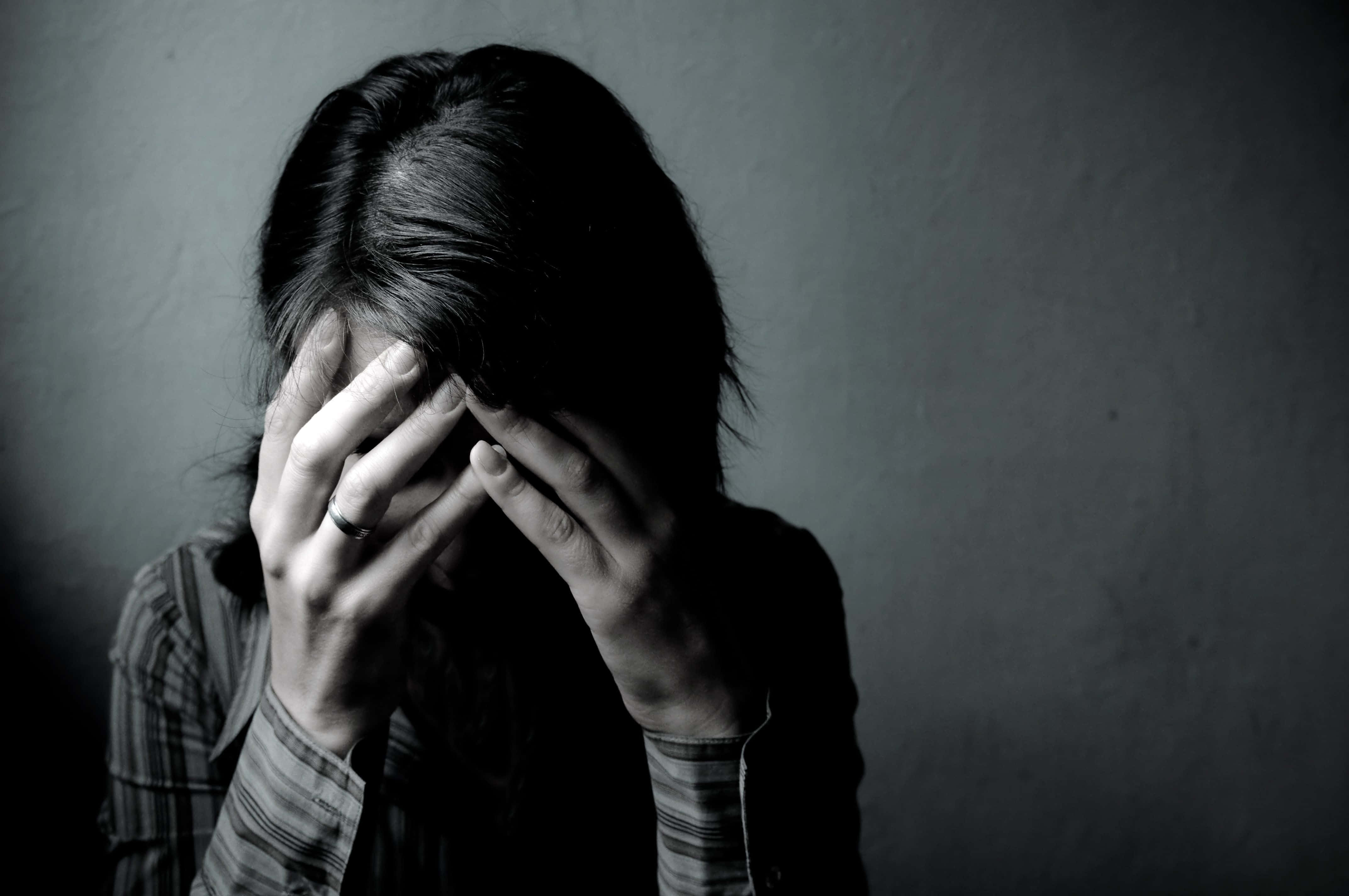 Depressed 桌布 壁紙 — 一個灰色調的人用雙手遮住臉，靠著素牆，傳達深深的痛苦或疲憊。