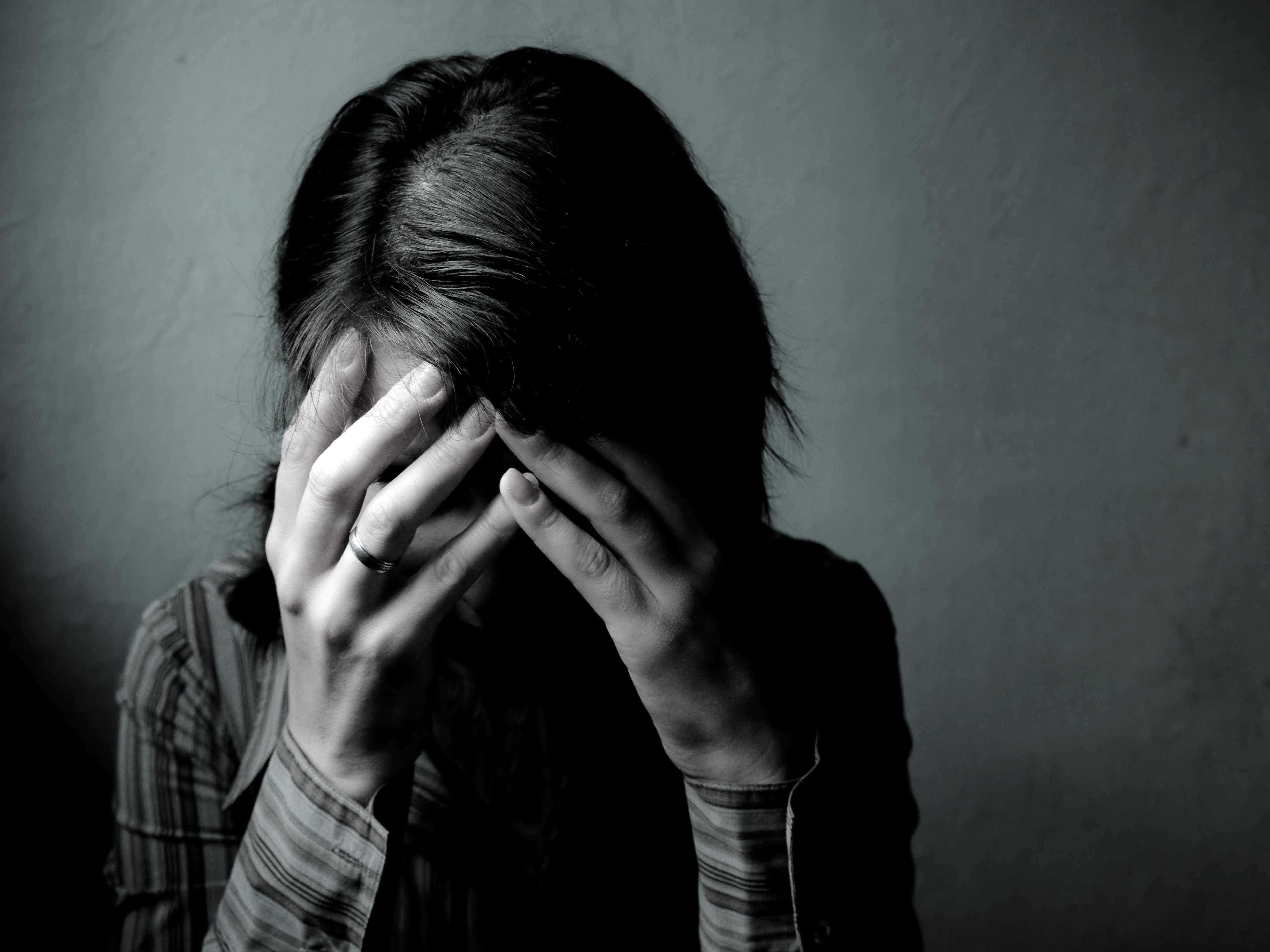 Depressed 桌布 壁紙 — 一個灰階的人用雙手遮住臉，靠著素色牆壁，傳達出深深的痛苦或絕望。