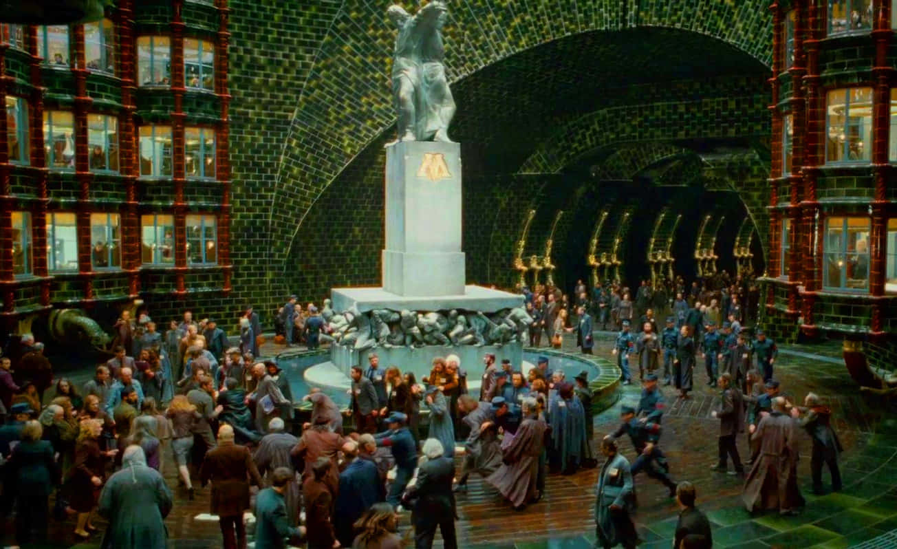 The Ministry Of Magic 桌布 壁紙 — 一個熙熙攘攘的巫師庭院，中央有一座雕像，拱形磚隧道下聚集著穿長袍的人群。