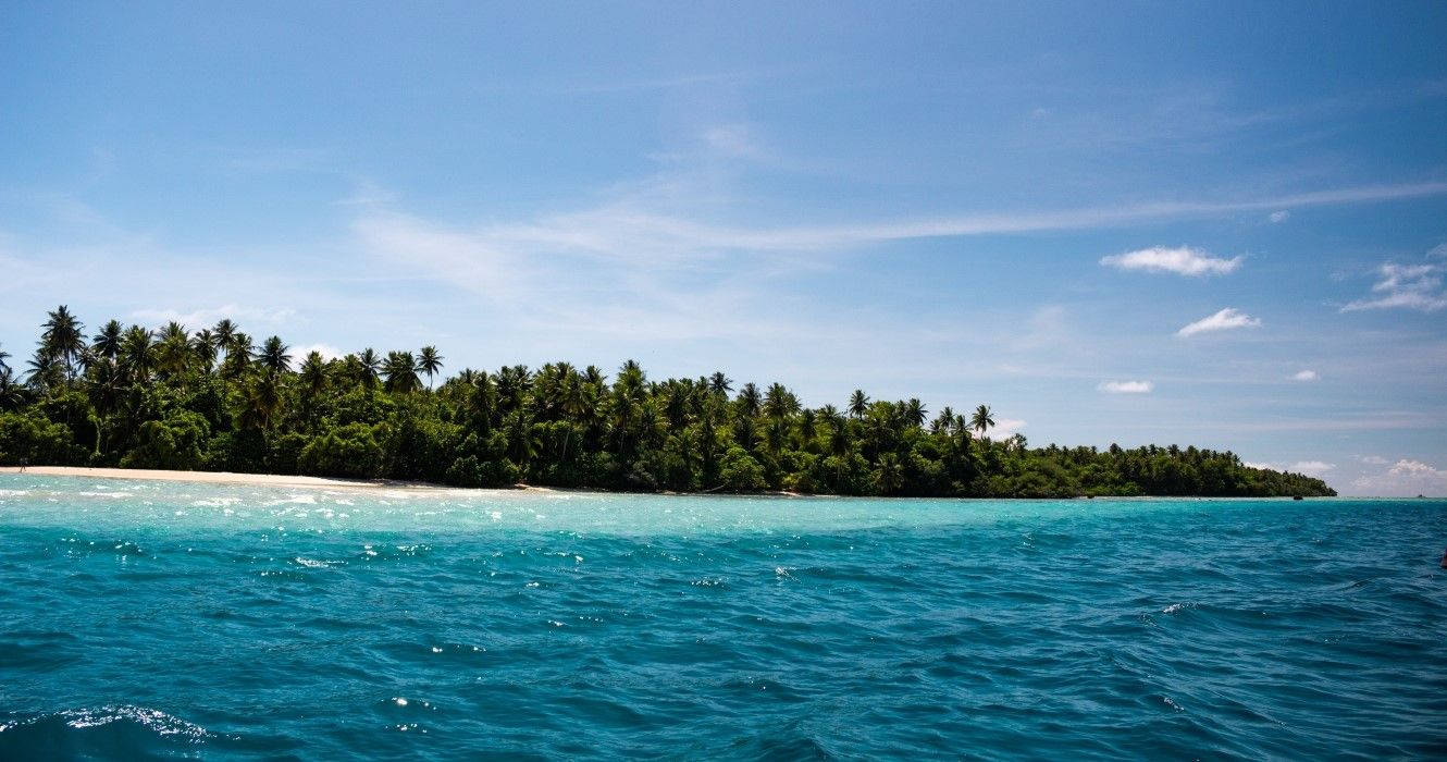 Micronesia 桌布 壁紙 — 一個熱帶島嶼，擁有茂密的棕櫚樹和白色沙灘，周圍是充滿活力的藍綠色海洋，上方是清澈的藍天。