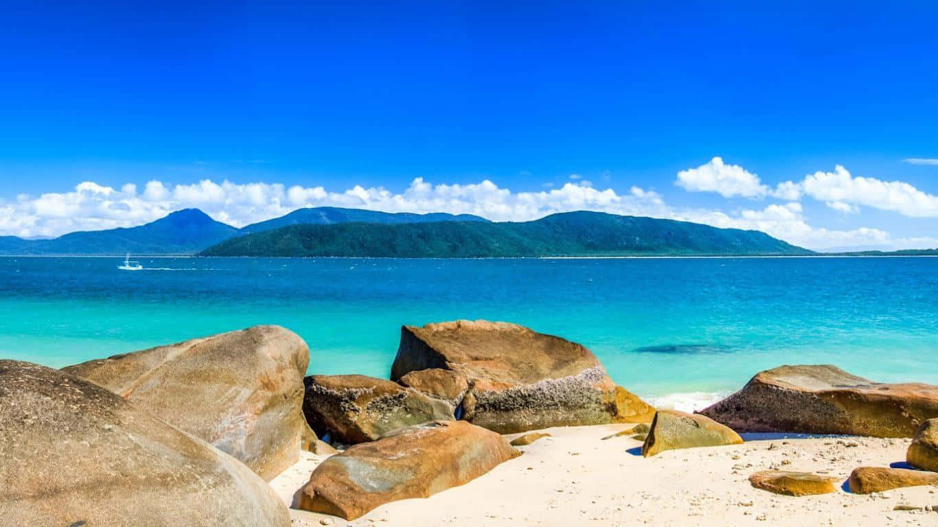 720p Beach 桌布 壁紙 — 一個熱帶海灘，有碧綠的海水和巨大的岩石，在明亮的藍天下有散落的雲朵。