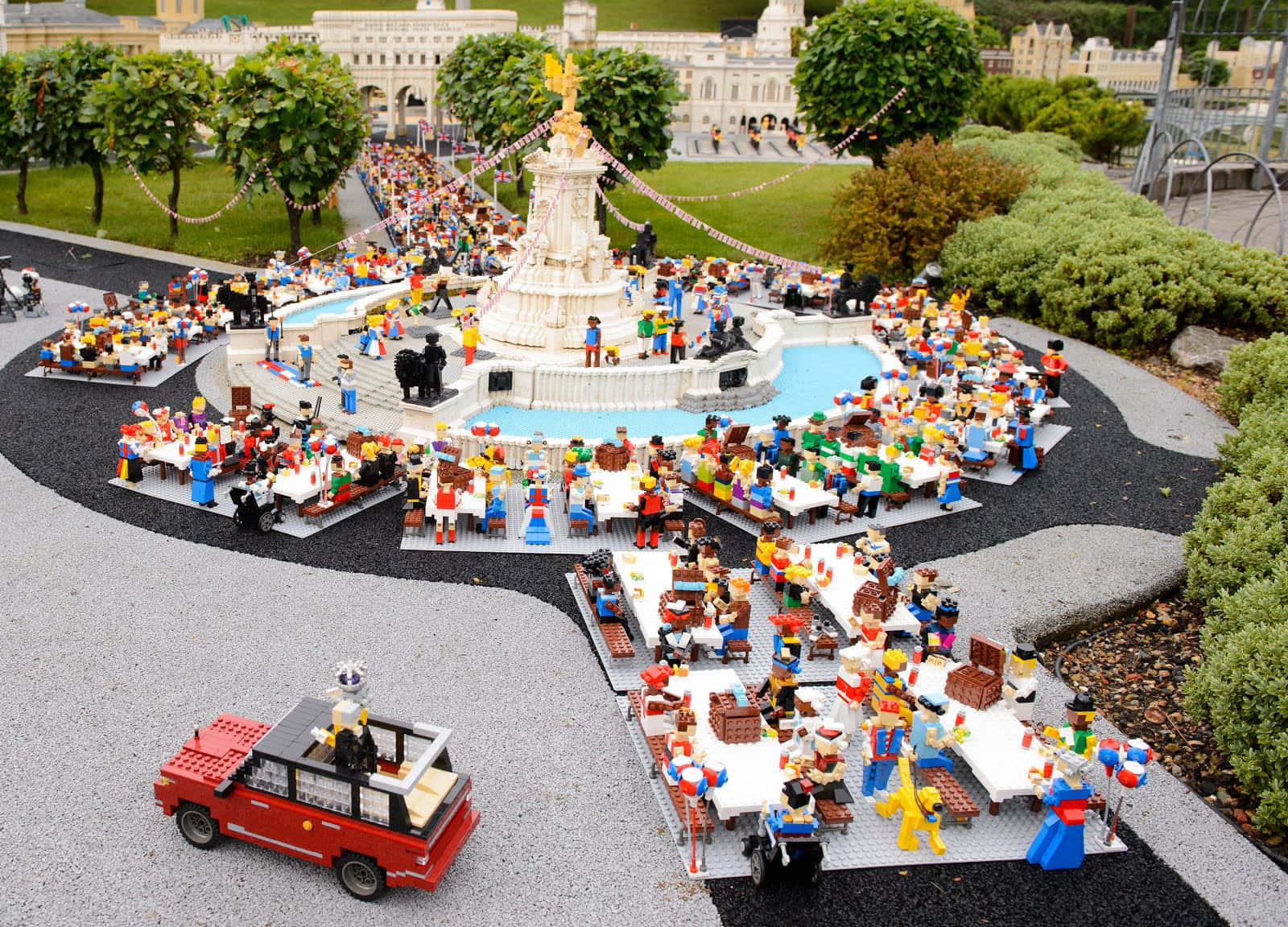 Legoland 桌布 壁紙 — 一個熱鬧的LEGO公園場景，小人物在中央噴泉周圍用餐，周圍環繞著綠植和一輛紅色LEGO汽車。