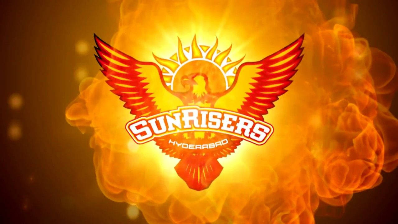 Sunrisers Hyderabad 桌布 壁紙 — 一個熾熱鳳凰標誌，展開翅膀和太陽爆發，在發光的橙色火焰背景上放射光芒。