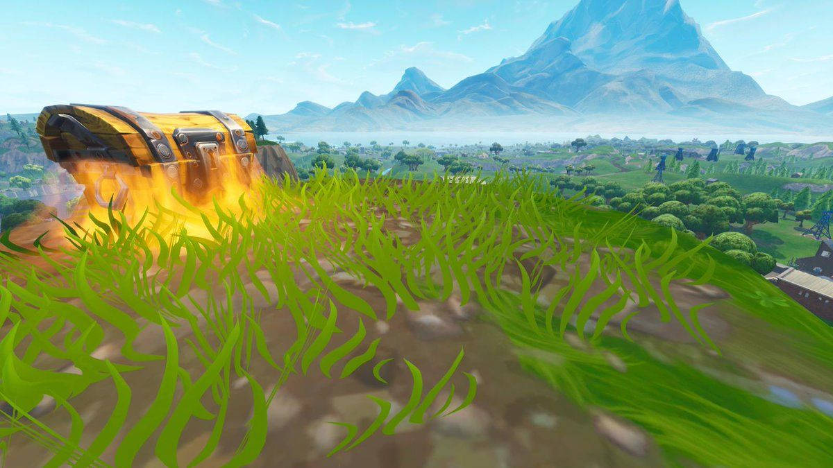 Fortnite 縮圖 桌布 壁紙 — 一個燃燒的寶箱放在翠綠的草地上，遠山在清澈的藍天下。