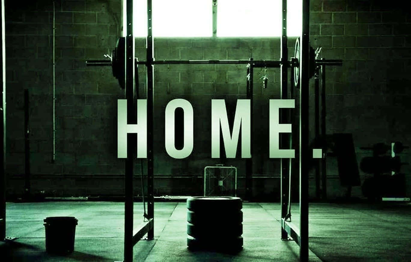 健身房 桌布 壁紙 — 一個燈光昏暗的健身房，在磚牆上發光的「HOME.」標誌下有一個槓鈴和啞鈴。