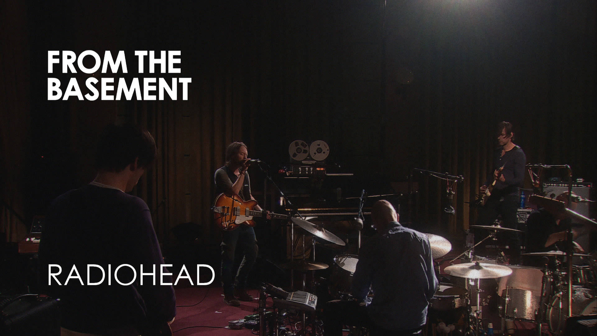 band 桌布 壁紙 — 一個燈光昏暗的地下室音樂會，Radiohead 在單一聚光燈下與吉他手、鼓手和主唱進行現場表演。