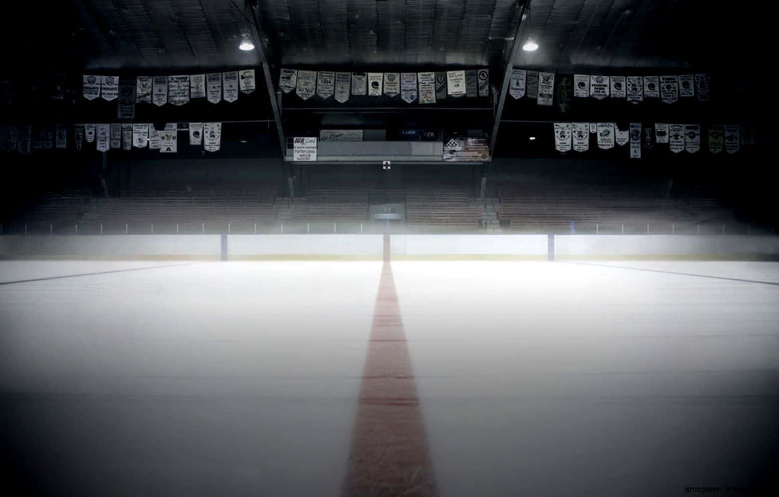 hockey 桌布 壁紙 — 一個燈光昏暗的室內冰球場，紅色中線延伸向空蕩的看台和懸掛的橫幅。