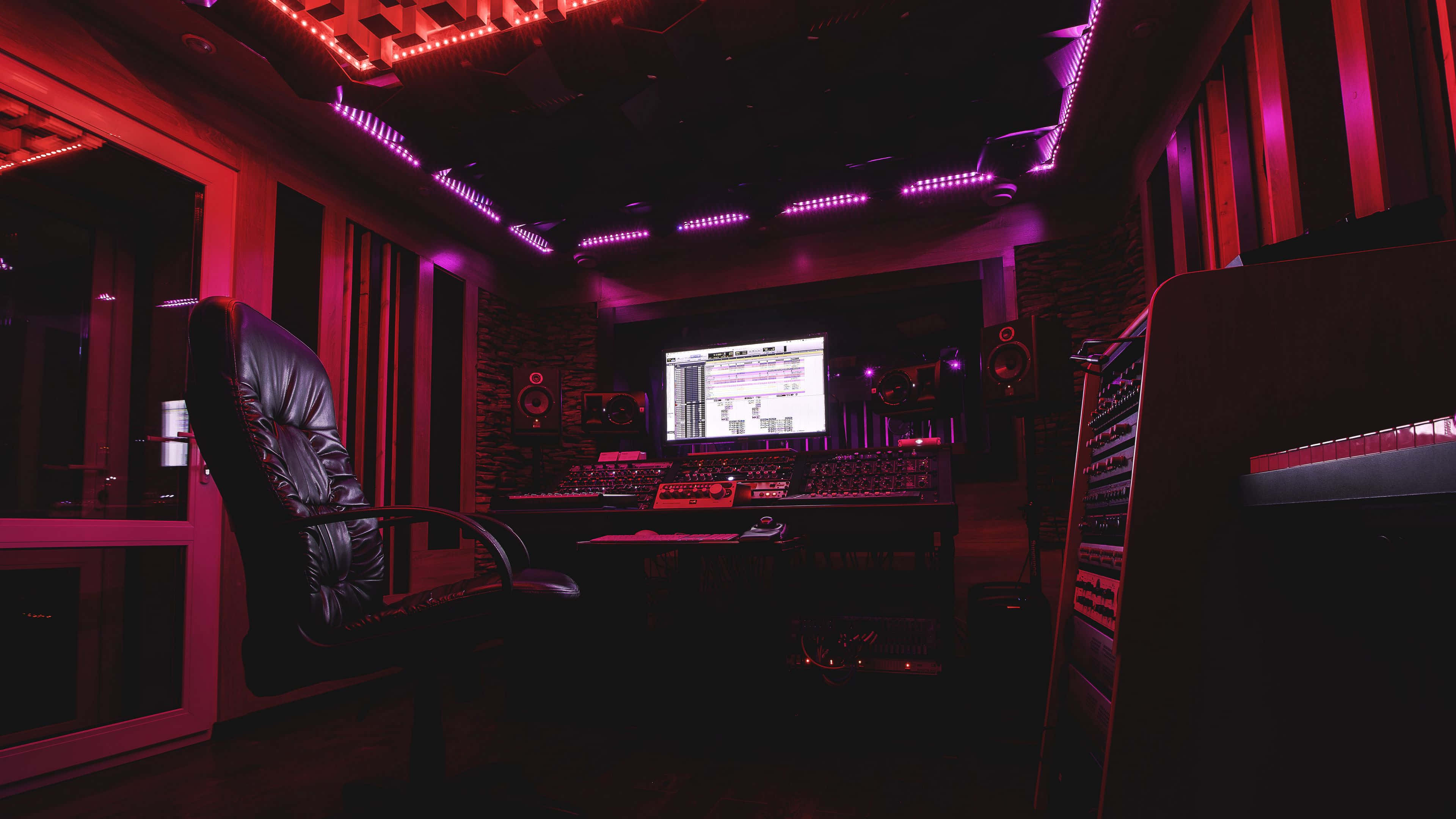Studio 桌布 壁紙 — 一個燈光昏暗的專業音樂工作室，沐浴在鮮豔的紅色和紫色LED燈光中，配有隔音牆和大型混音台。