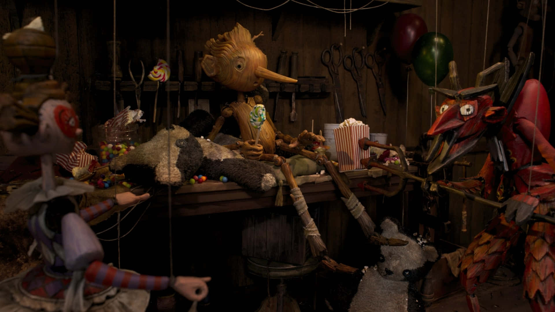 Guillermo Del Toro's Pinocchio 桌布 壁紙 — 一個燈光昏暗的木偶劇院，充滿了木製懸絲木偶和散落的糖果，在一個雜亂的工作室裡。
