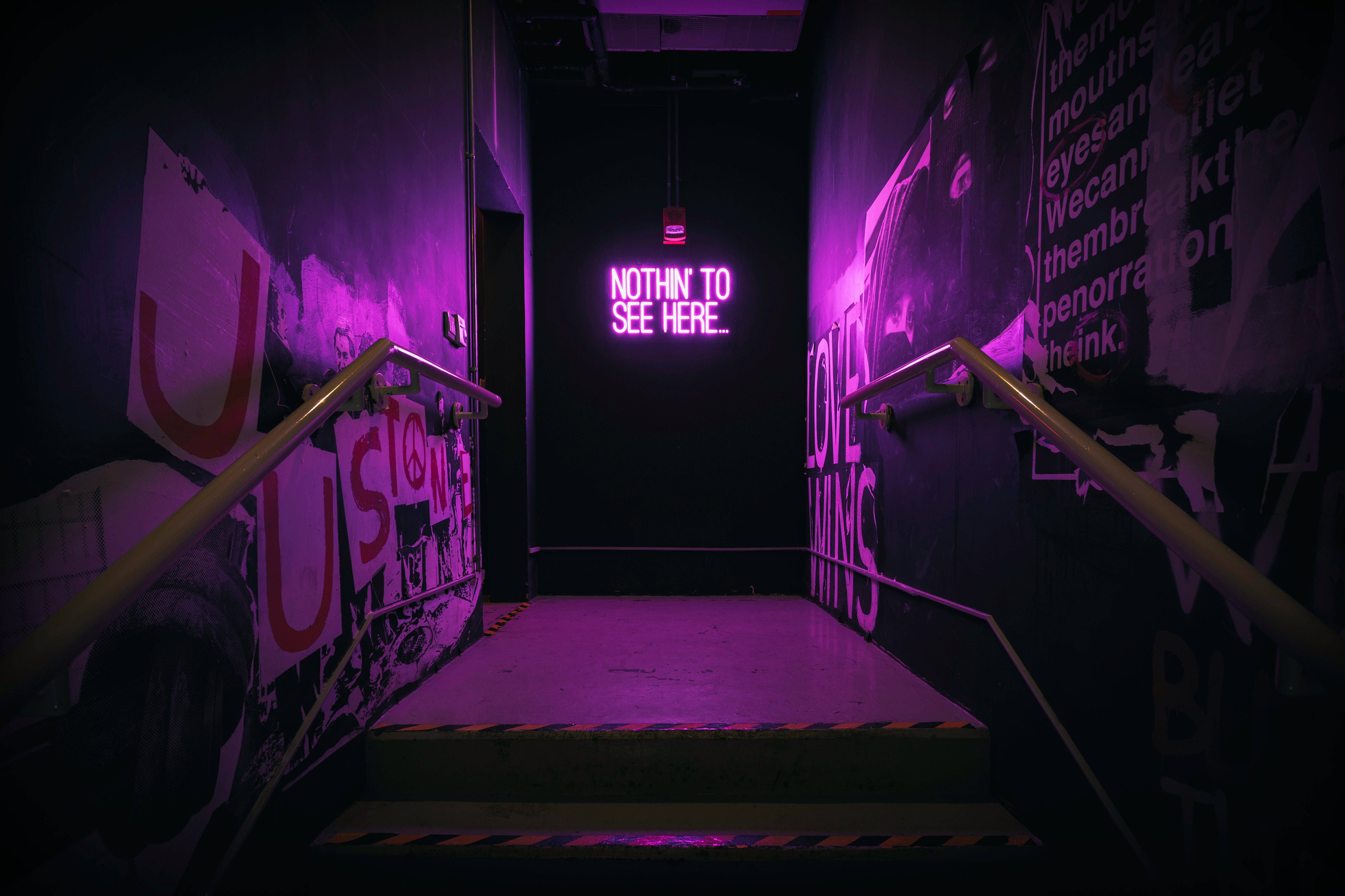 neon sign 桌布 壁紙 — 一個燈光昏暗的樓梯間，沐浴在紫色霓虹燈光中，牆壁上佈滿塗鴉，還有一個發光的標誌寫著 notthin to see here。
