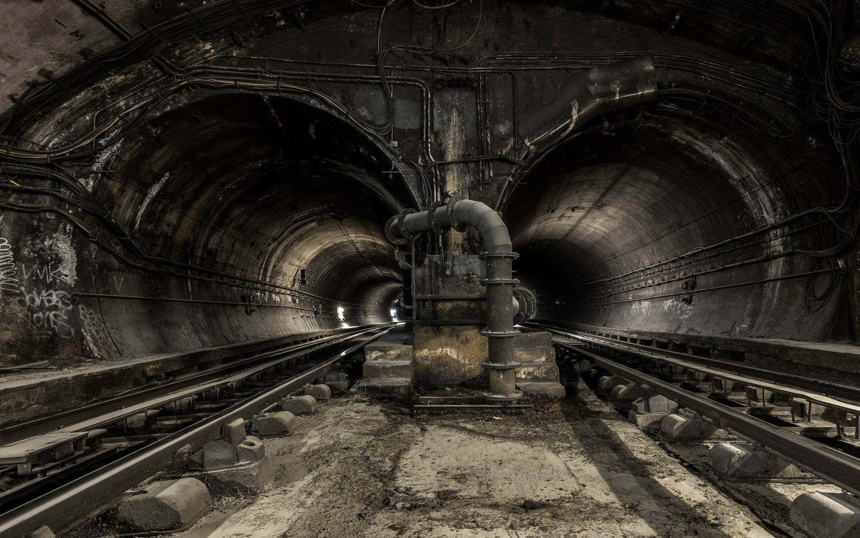 tunnel 桌布 壁紙 — 一個燈光昏暗的被廢棄地鐵隧道，生鏽的軌道、佈滿塗鴉的牆壁和暴露的管道，營造出一種粗獷的工業氛圍。
