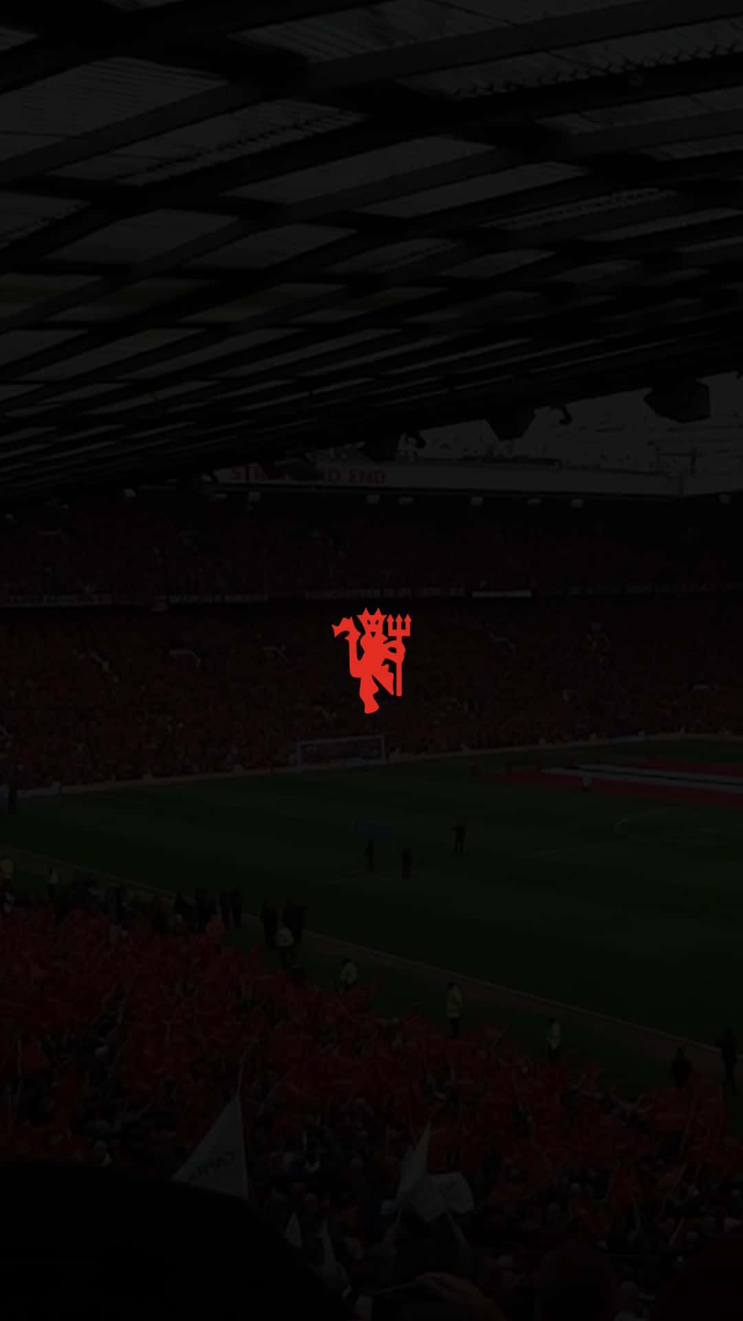 Manchester United iPhone 桌布 壁紙 — 一個燈光昏暗的足球場，擠滿了身穿紅色衣服的球迷，球場中央有一個發光的紅色魔鬼標誌。