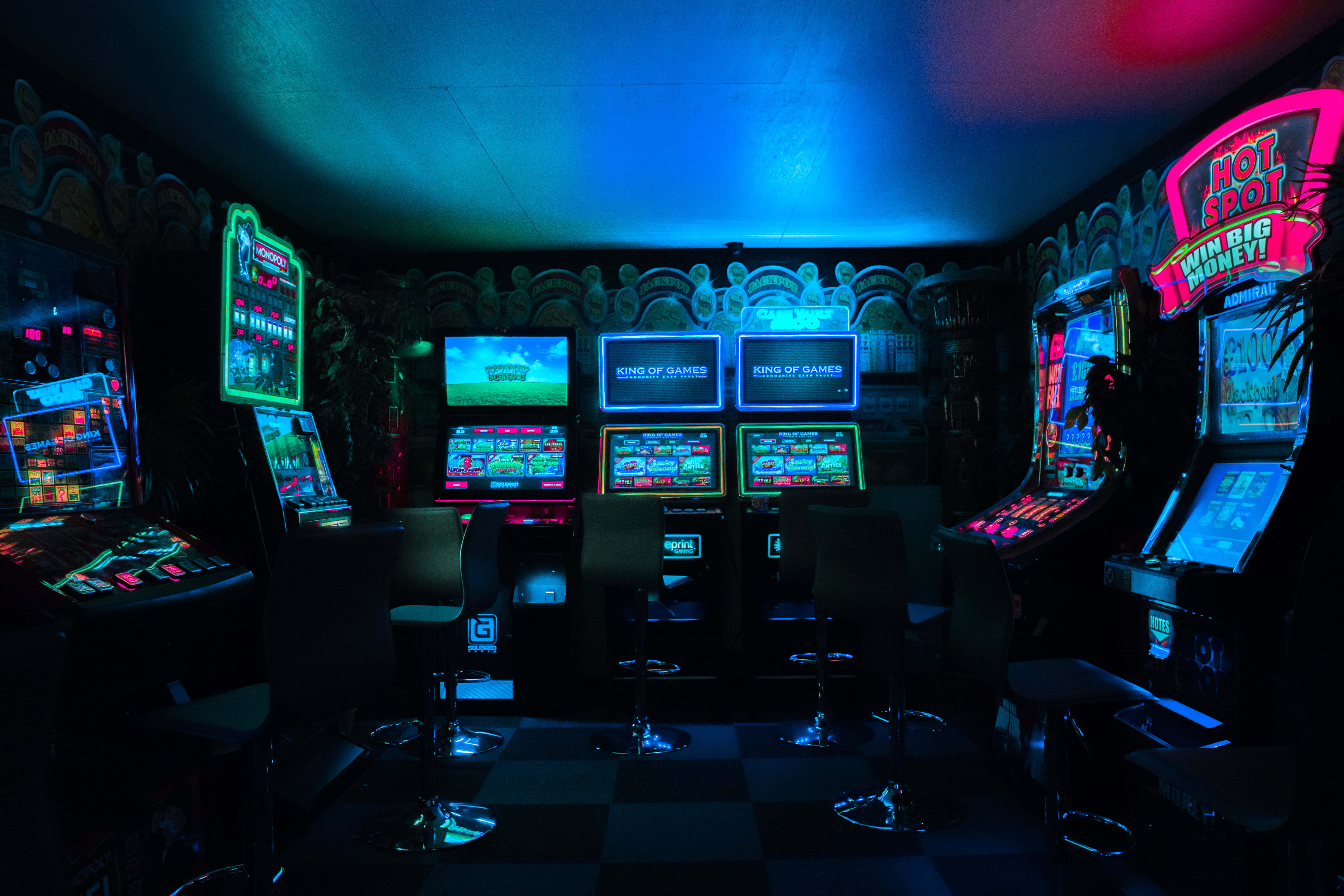 arcade 桌布 壁紙 — 一個燈光昏暗的遊戲機室，沐浴在復古遊戲機的霓虹光芒中，發光的螢幕下是棋盤格地板。