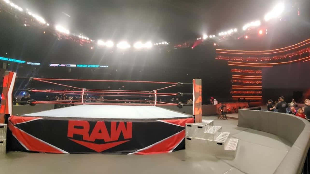 Wrestling Ring 桌布 壁紙 — 一個燈光璀璨的WWE RAW摔角擂台，位於座無虛席的場館中央，在戲劇性的舞台燈光下。